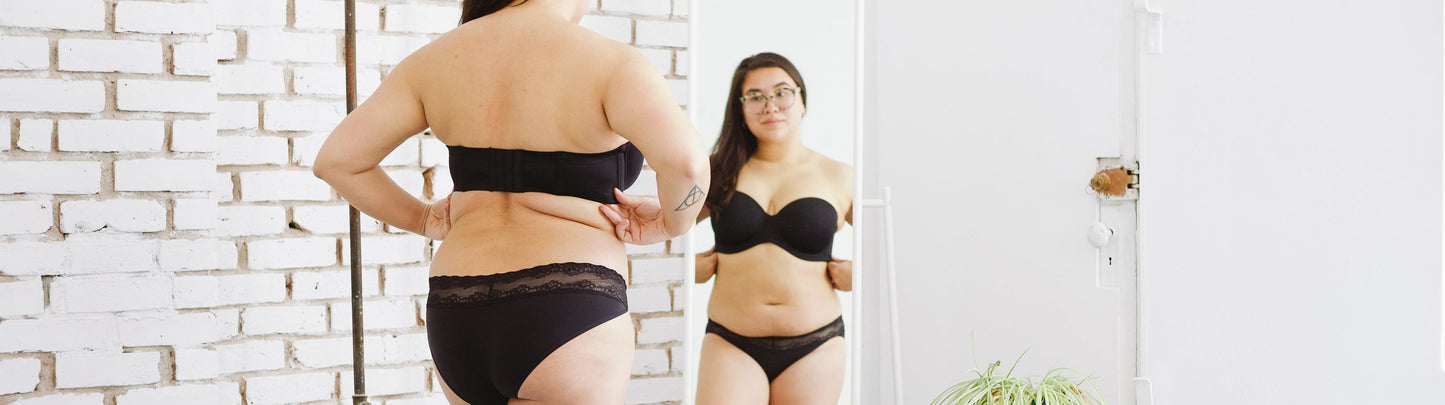 A person in a black strapless bra standing in front a mirror. Find solution bras and strapless bras at Forty Winks 