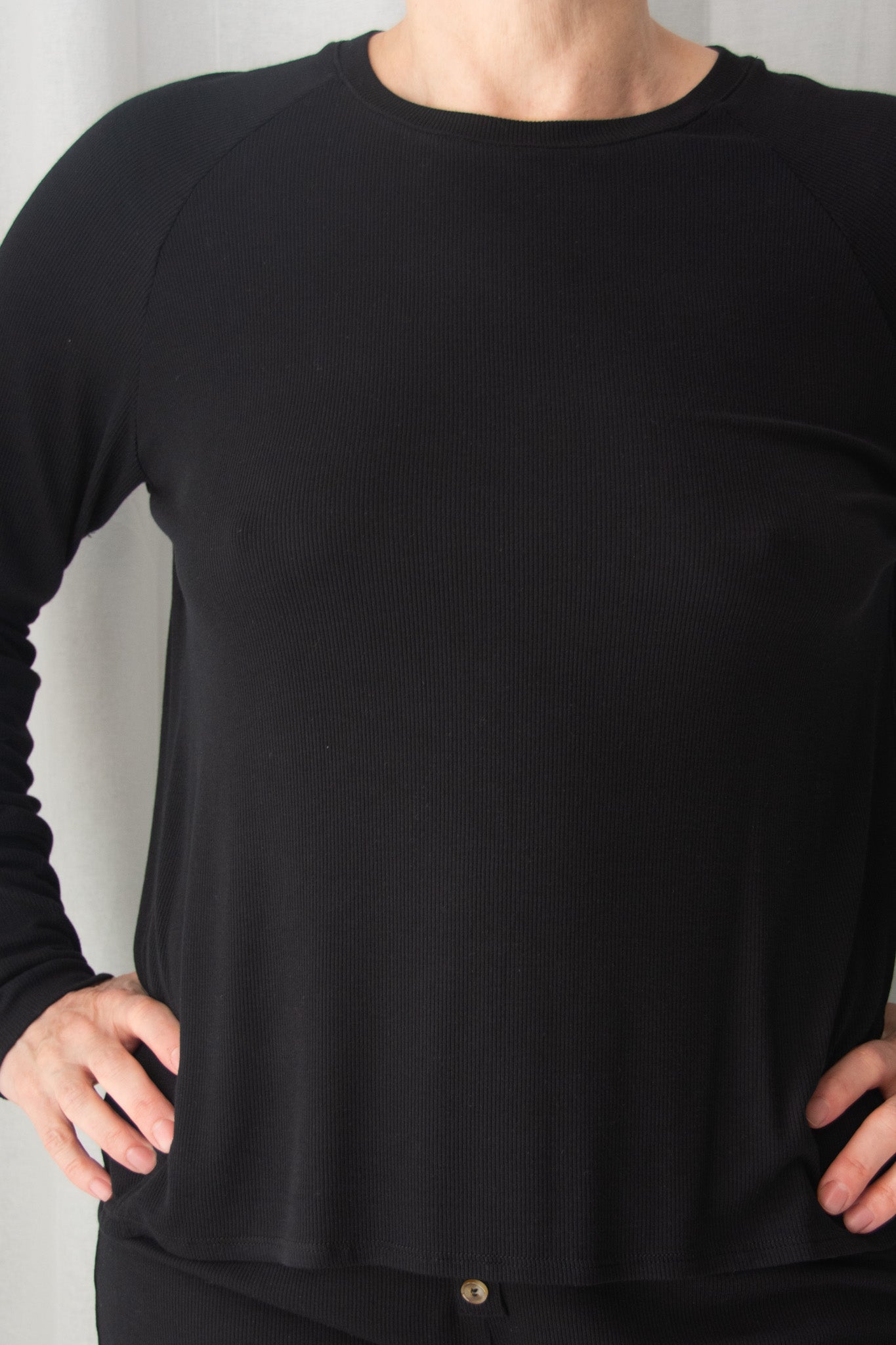 Black long-sleeve top worn by a person on a light gray background