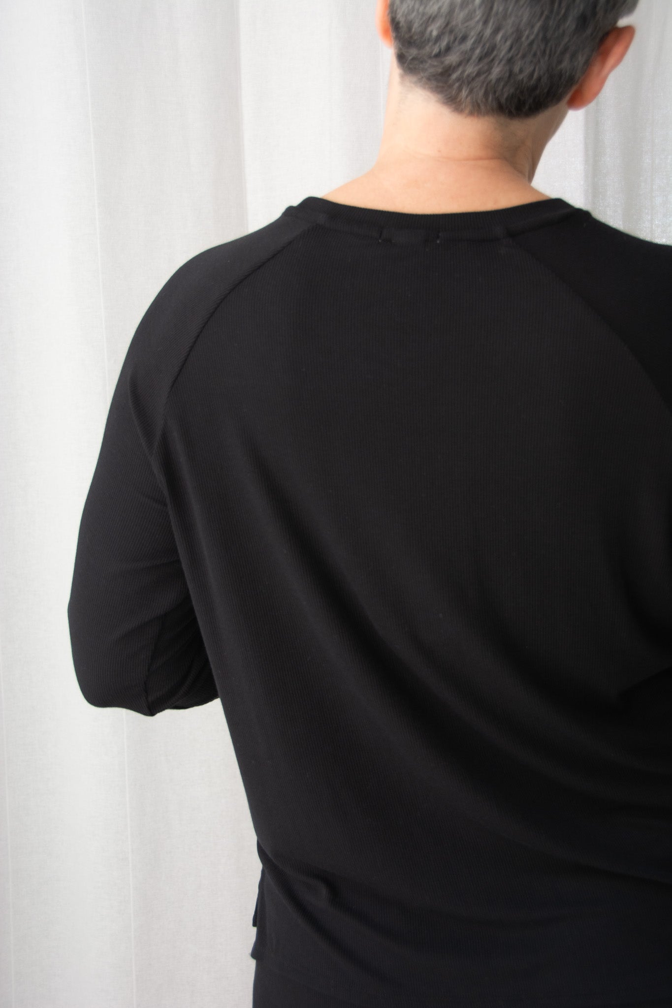 Person wearing a black long-sleeve shirt against a white curtain background
