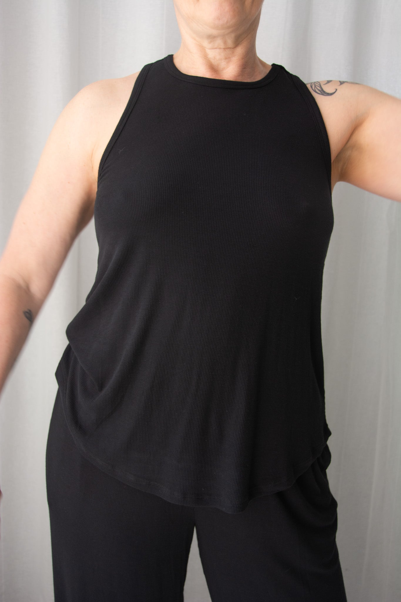 Person wearing a black sleeveless top and pants against a plain background