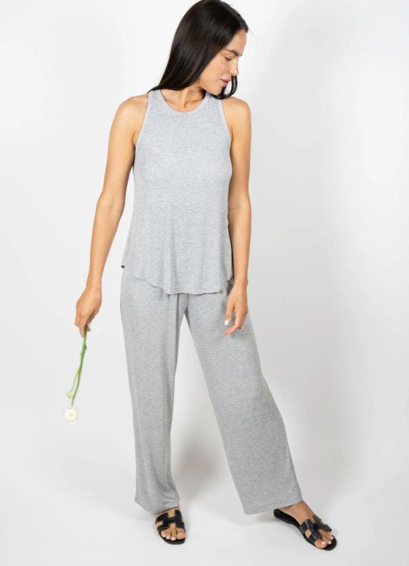 Woman wearing a gray sleeveless top and pants holding a white flower on a white background