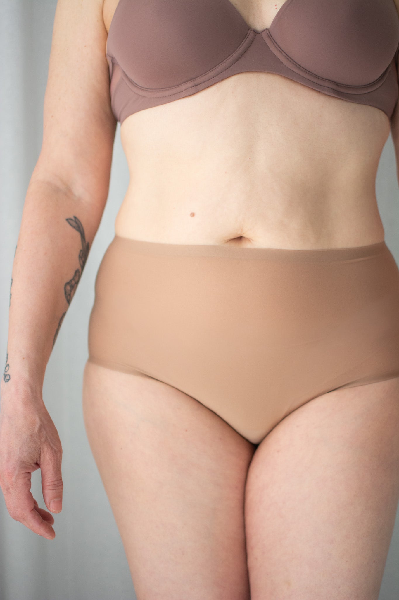 Person wearing a brown bra and beige underwear against a plain background