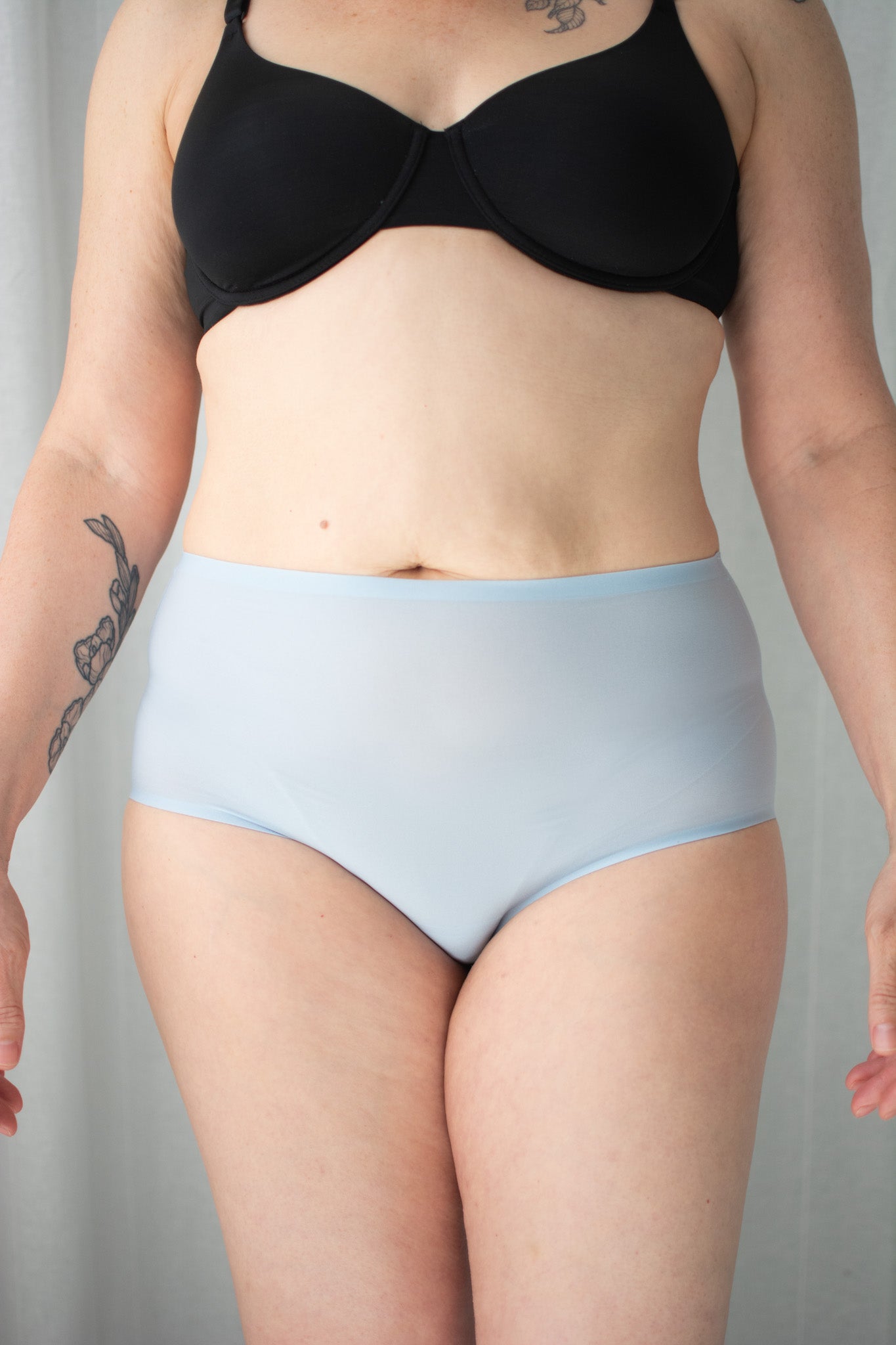 Person wearing blue underwear and black bra against a neutral background.