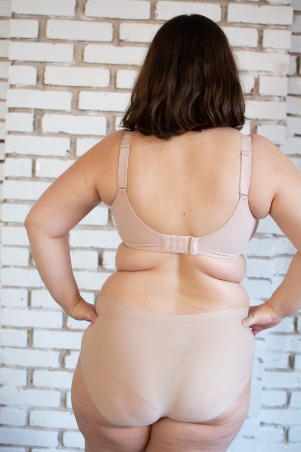 Chantelle Comfort Chic back smoothing T-shirt bra in soft pink, back view on a model, close-up, on brick wall background.