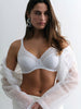 Woman wearing a white lace bralette with sheer fabric draped over her shoulders against a plain background.