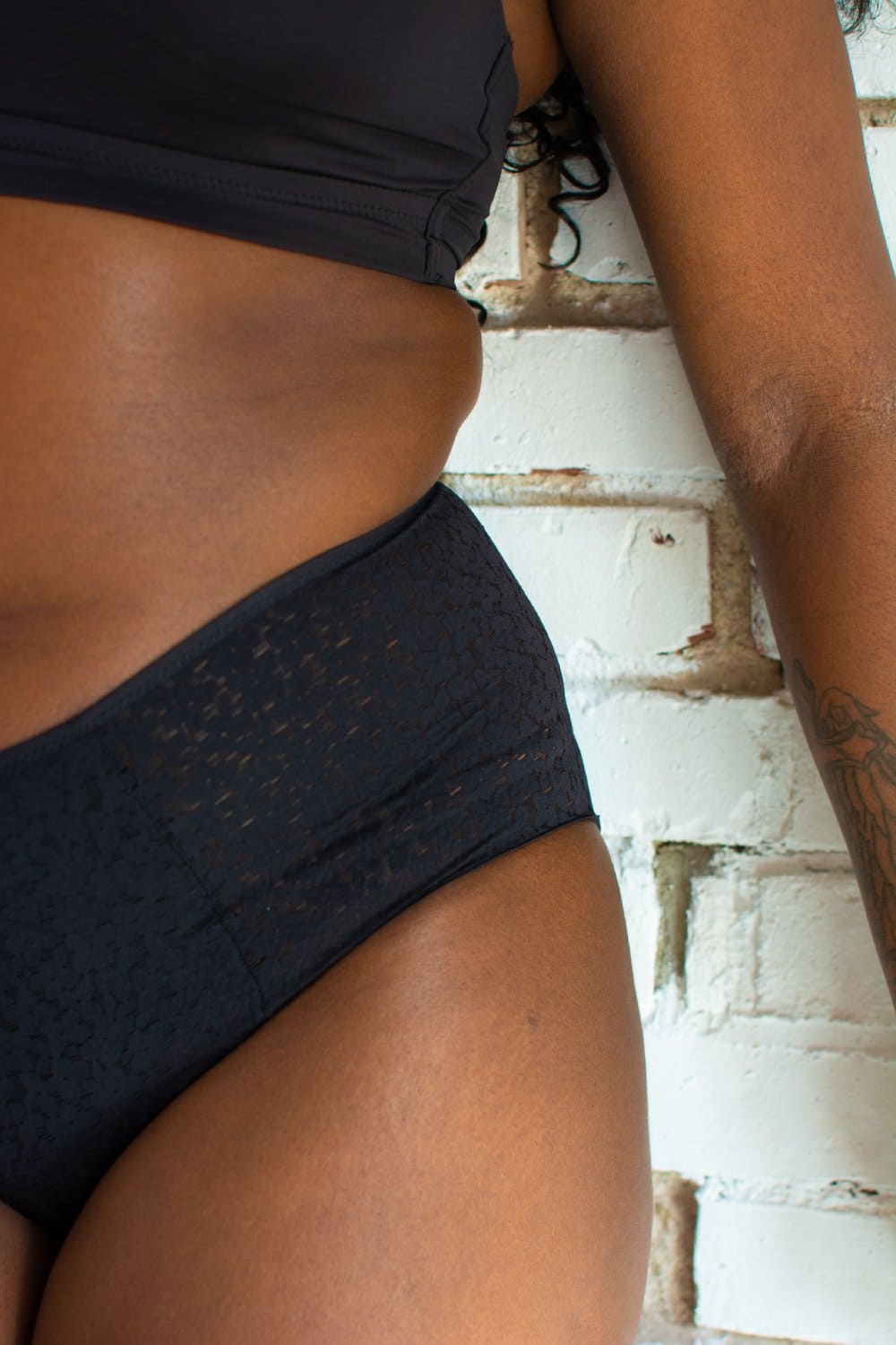 Chantelle norah high waist brief in black, close-up on a model, brick wall background.