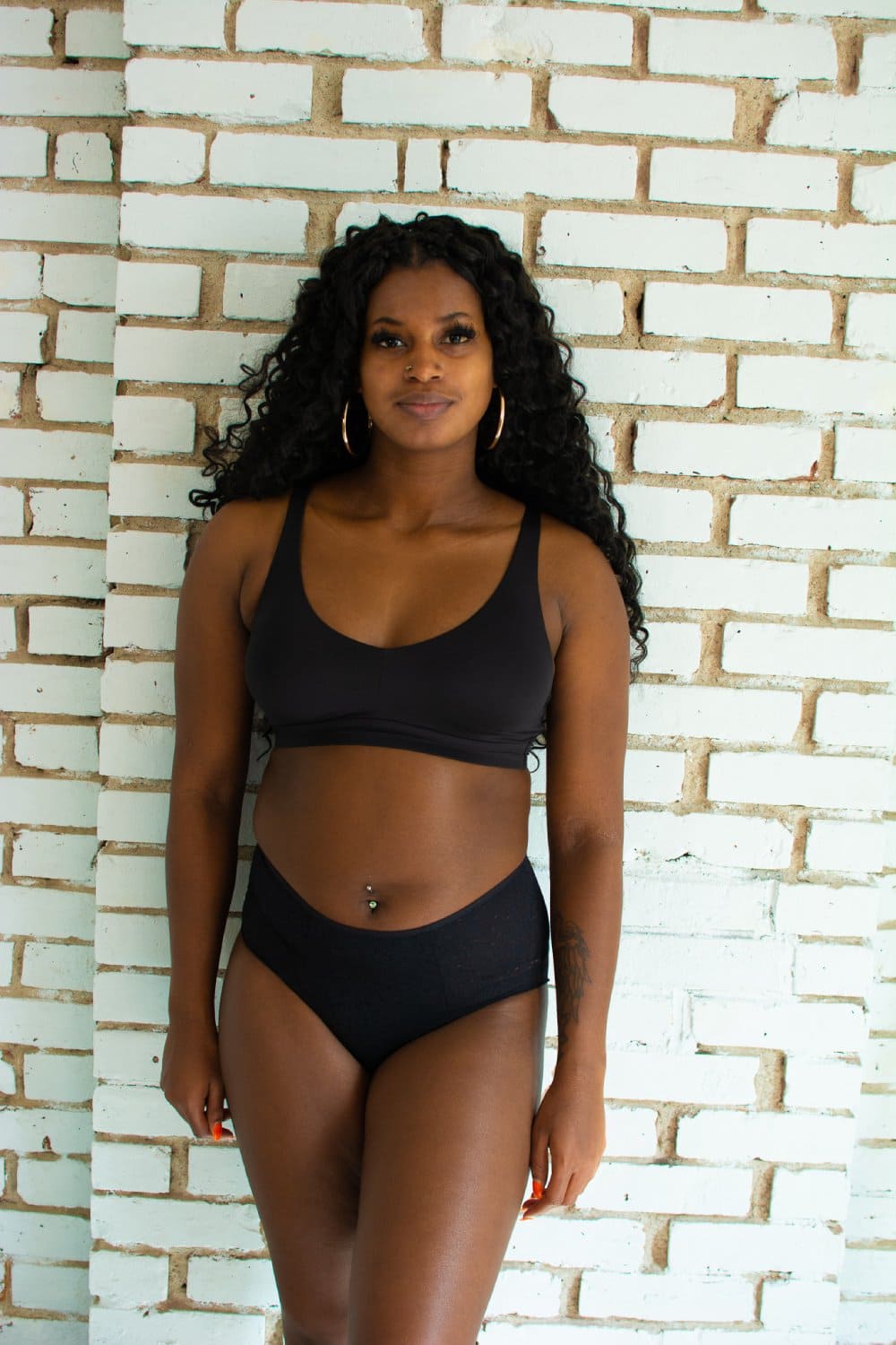Chantelle norah high waist brief in black, front view on a model, full-body, brick wall background.