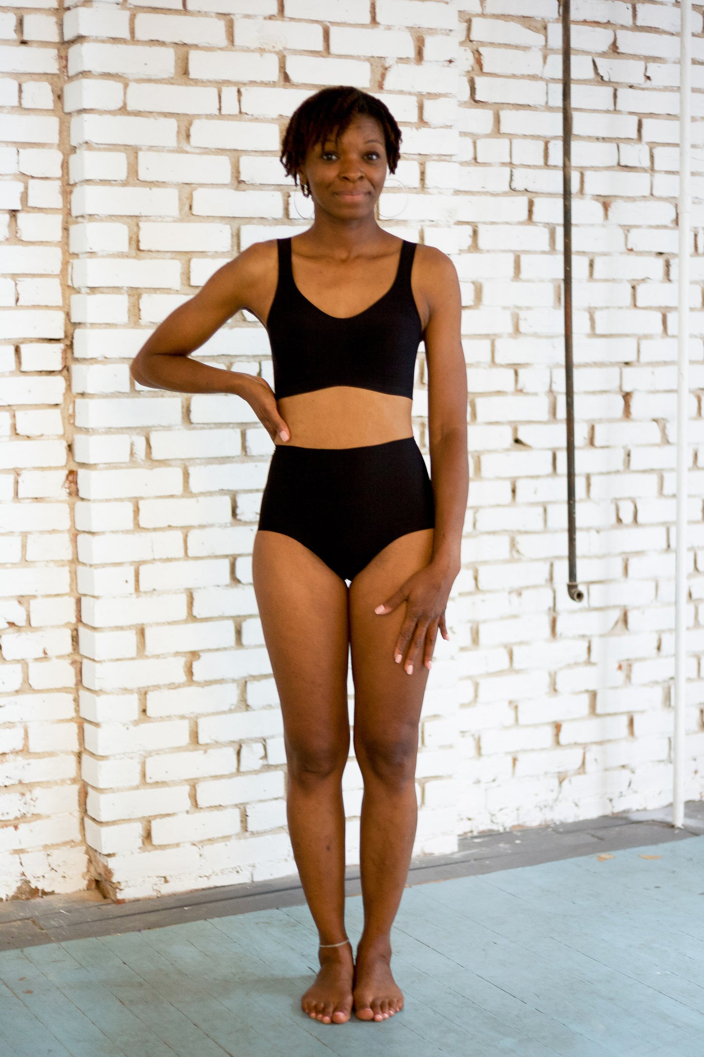 Person wearing black underwear against a white brick wall.