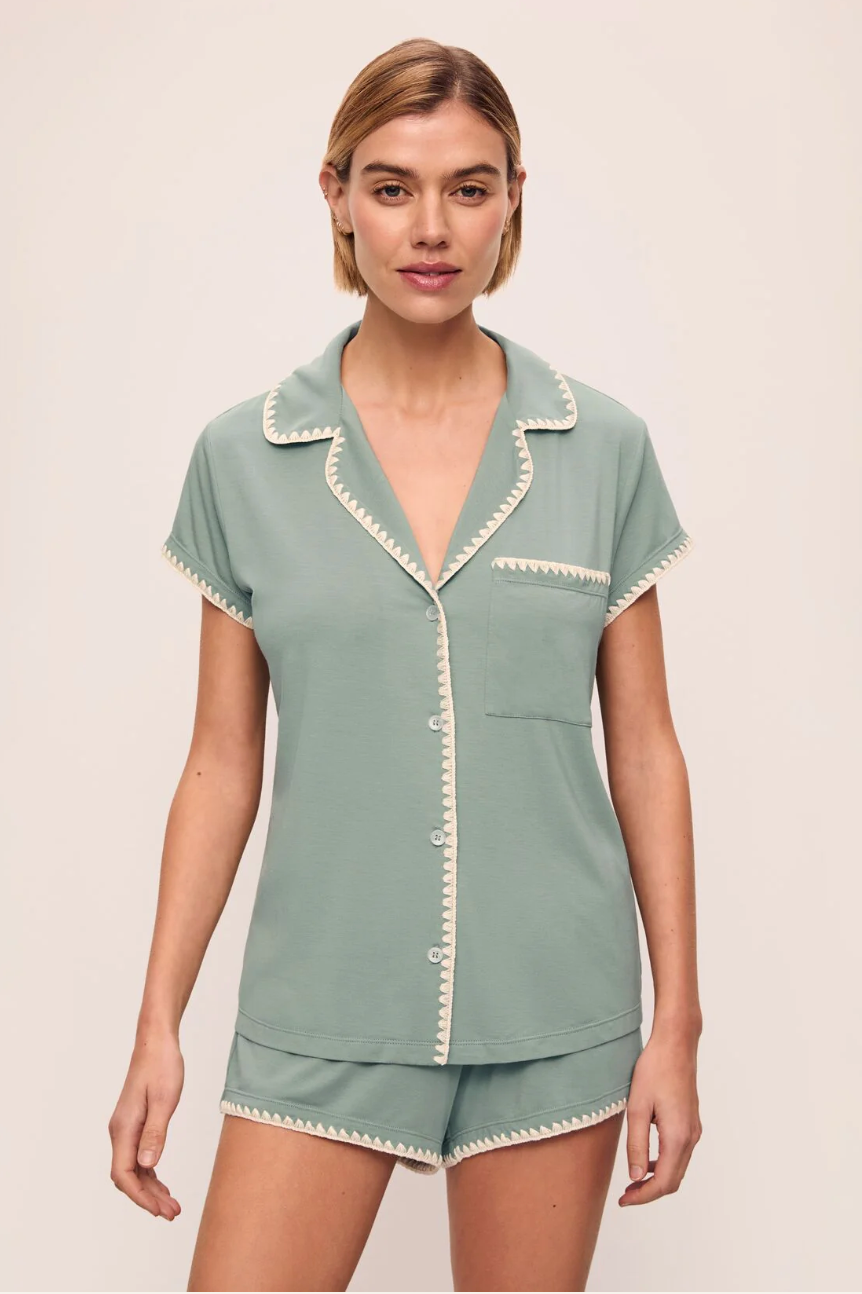 A woman wearing a green short-sleeved pajama set with contrast whipstitching and shorts that hit high on the thigh.