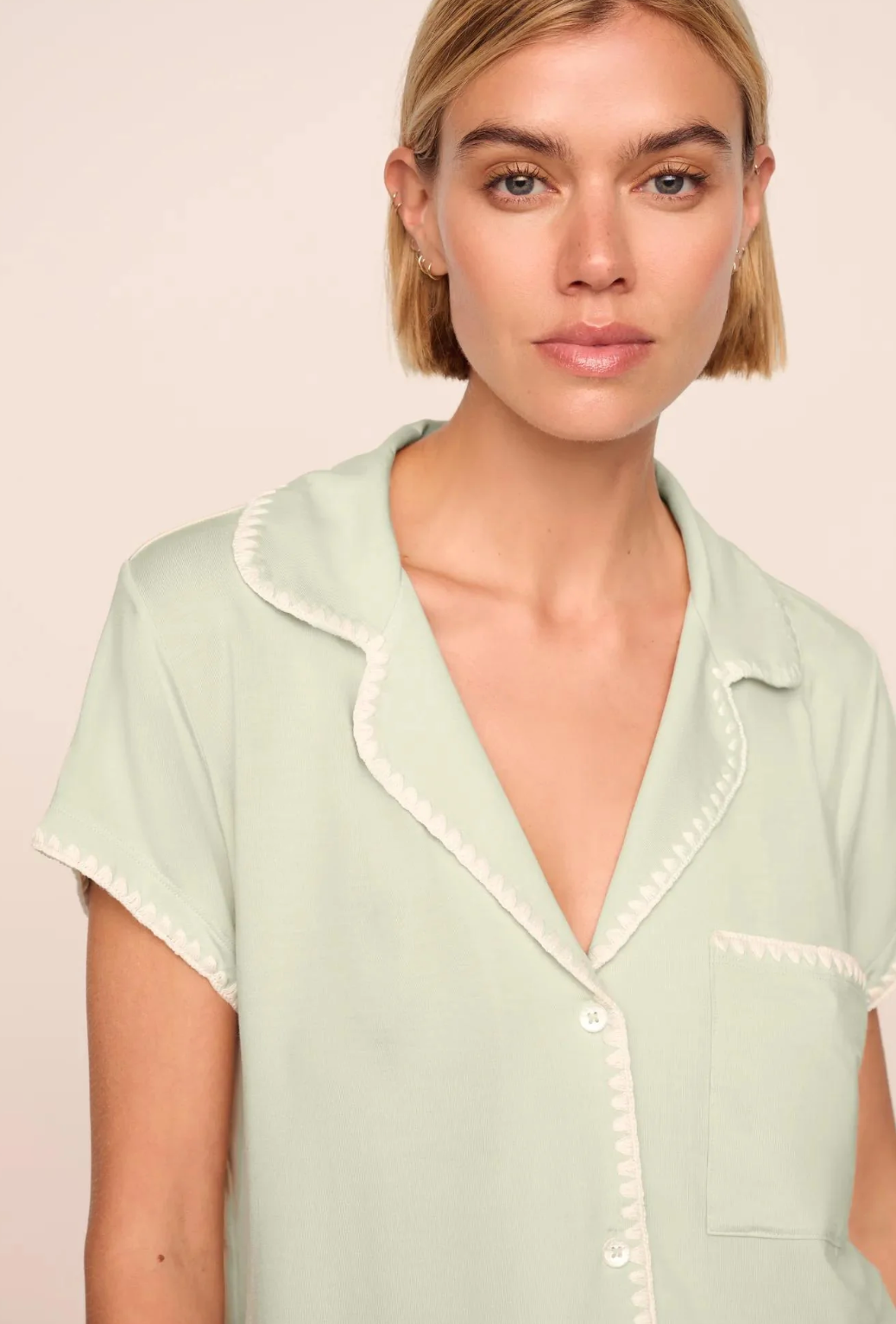 Woman wearing a light green shirt with white trim on a beige background