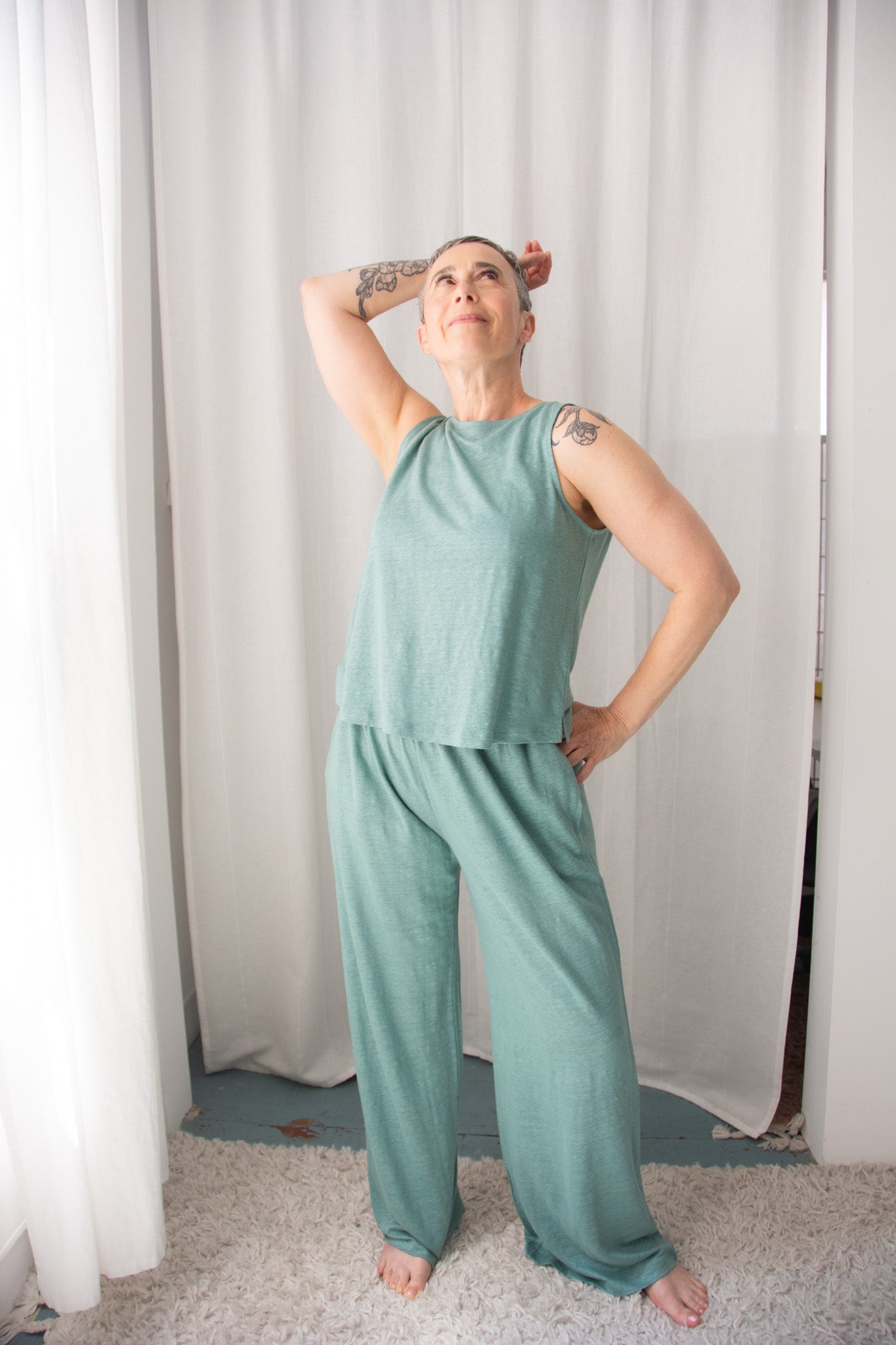 Person wearing a teal sleeveless top and pants against a white curtain background