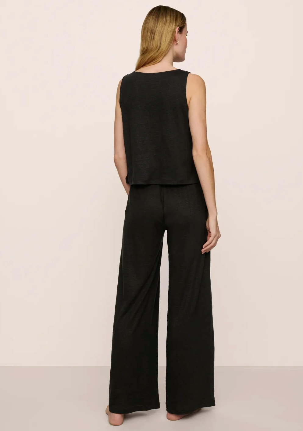 Woman wearing a black sleeveless top and wide-leg pants on a plain background