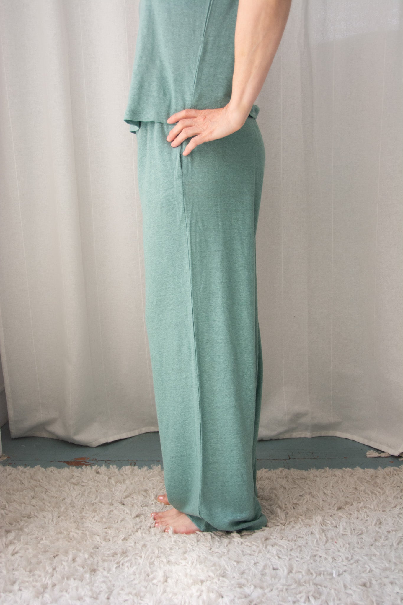 Person wearing teal pajama pants standing against a white curtain.