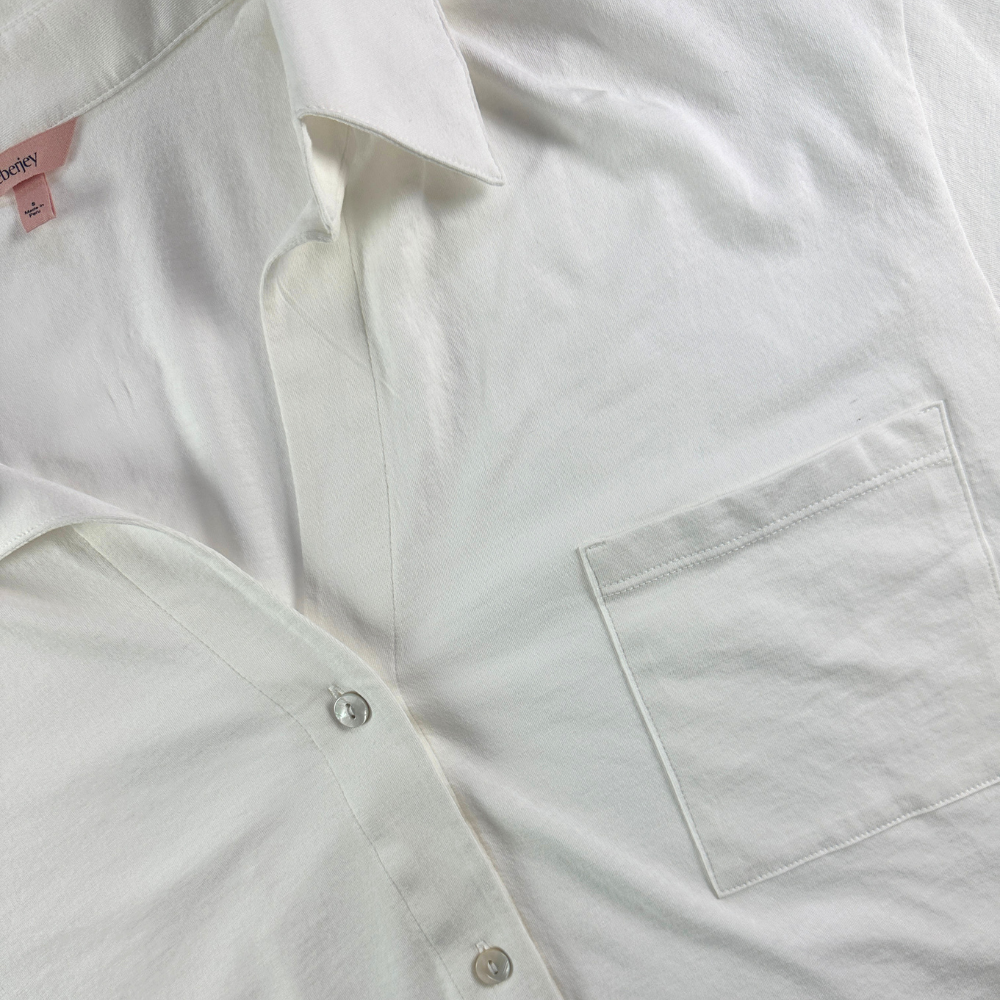 A close-up of a white long-sleeve button-up shirt with a single chest pocket, laid flat.