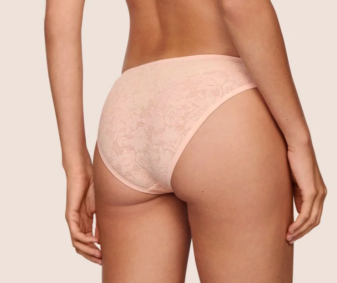 Rear view of a model wearing light pink lace high-waisted briefs against a plain beige background.