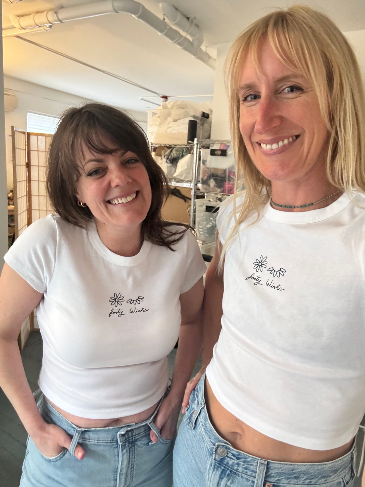Two women wearing white t-shirts with a logo, standing close together indoors.