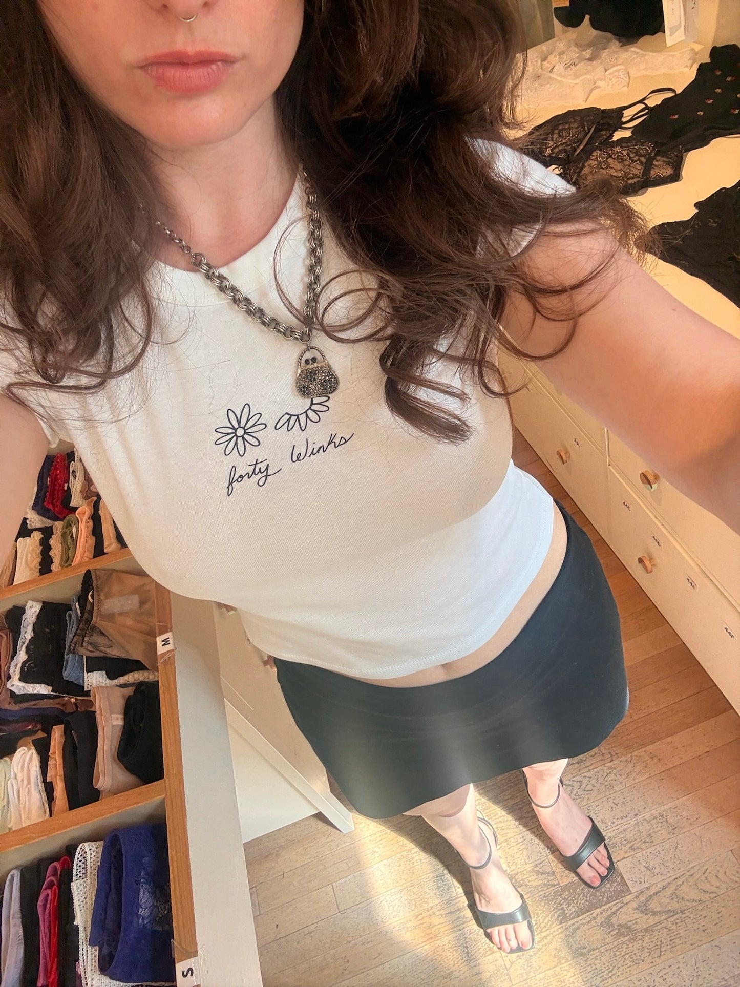 Woman wearing a white t-shirt with text and a necklace in a room with shelves of clothing.