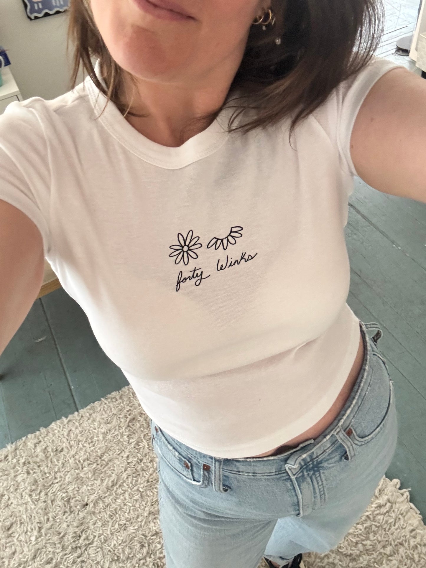 Person wearing a white shirt with text and light blue jeans on a carpeted floor.