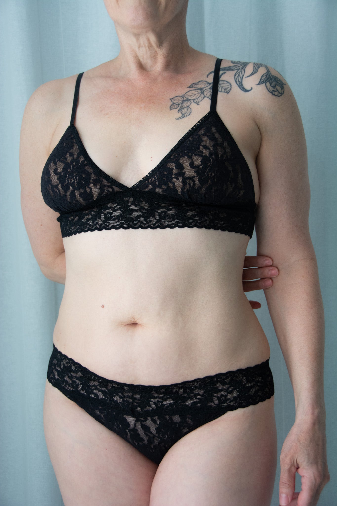 Person wearing a black lace bra and panties set against a light blue background