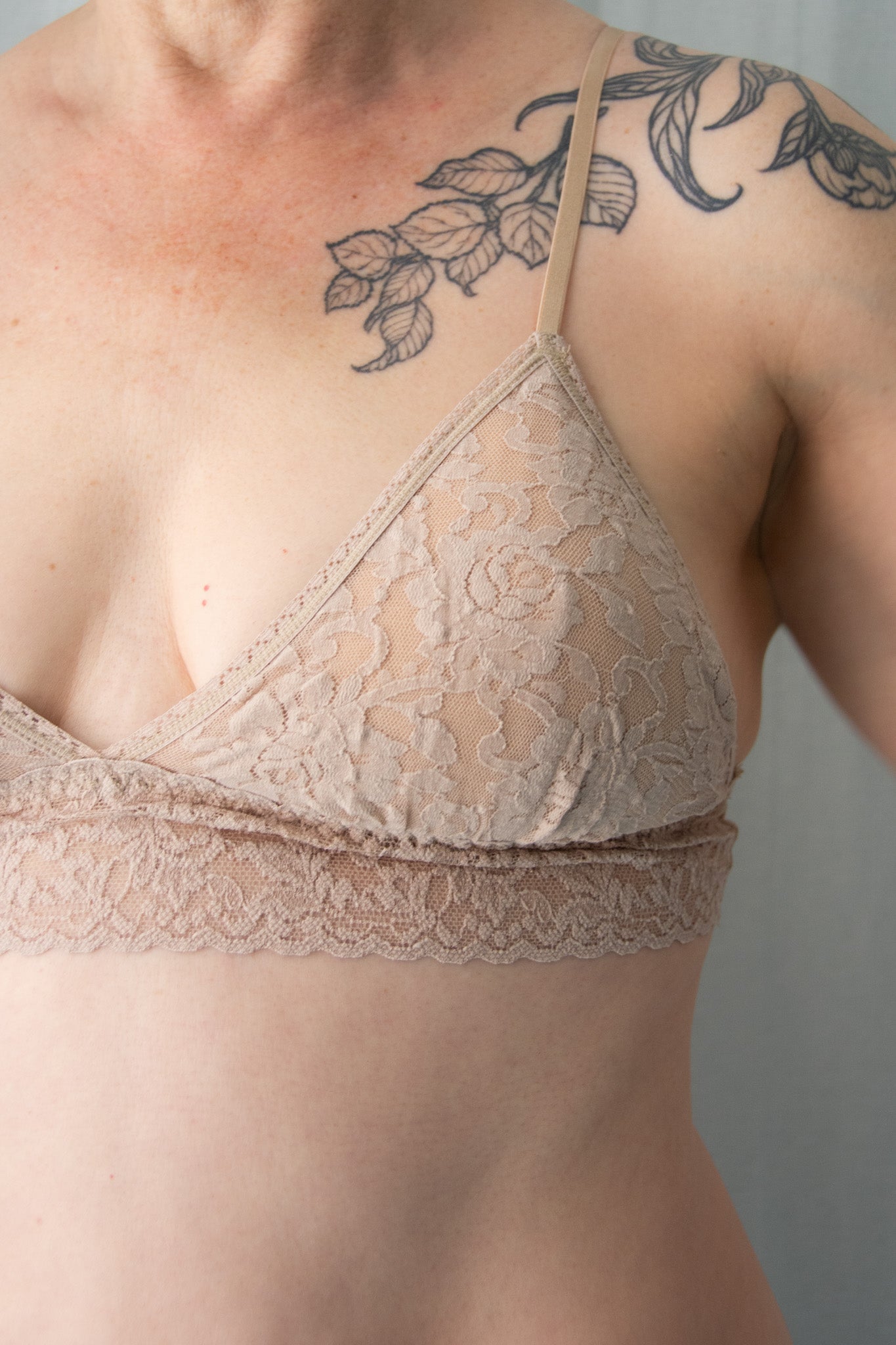 Person wearing a beige lace bra against a neutral background