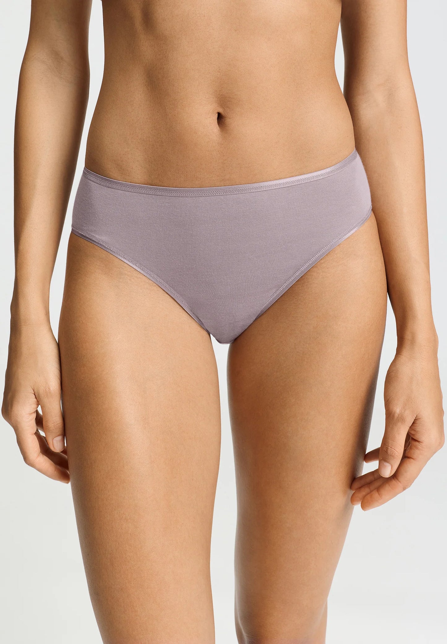 A model wearing a ribbed, high-waisted bikini bottom in a muted mauve or dusty lavender color, shown from the waist to the upper thighs against a light gray studio background.