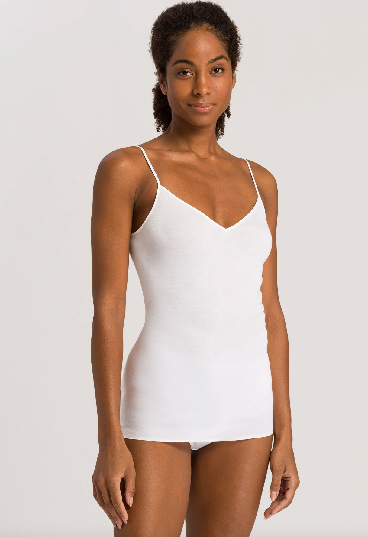 A woman modeling a white spaghetti-strap camisole tank top against a light gray studio background.
