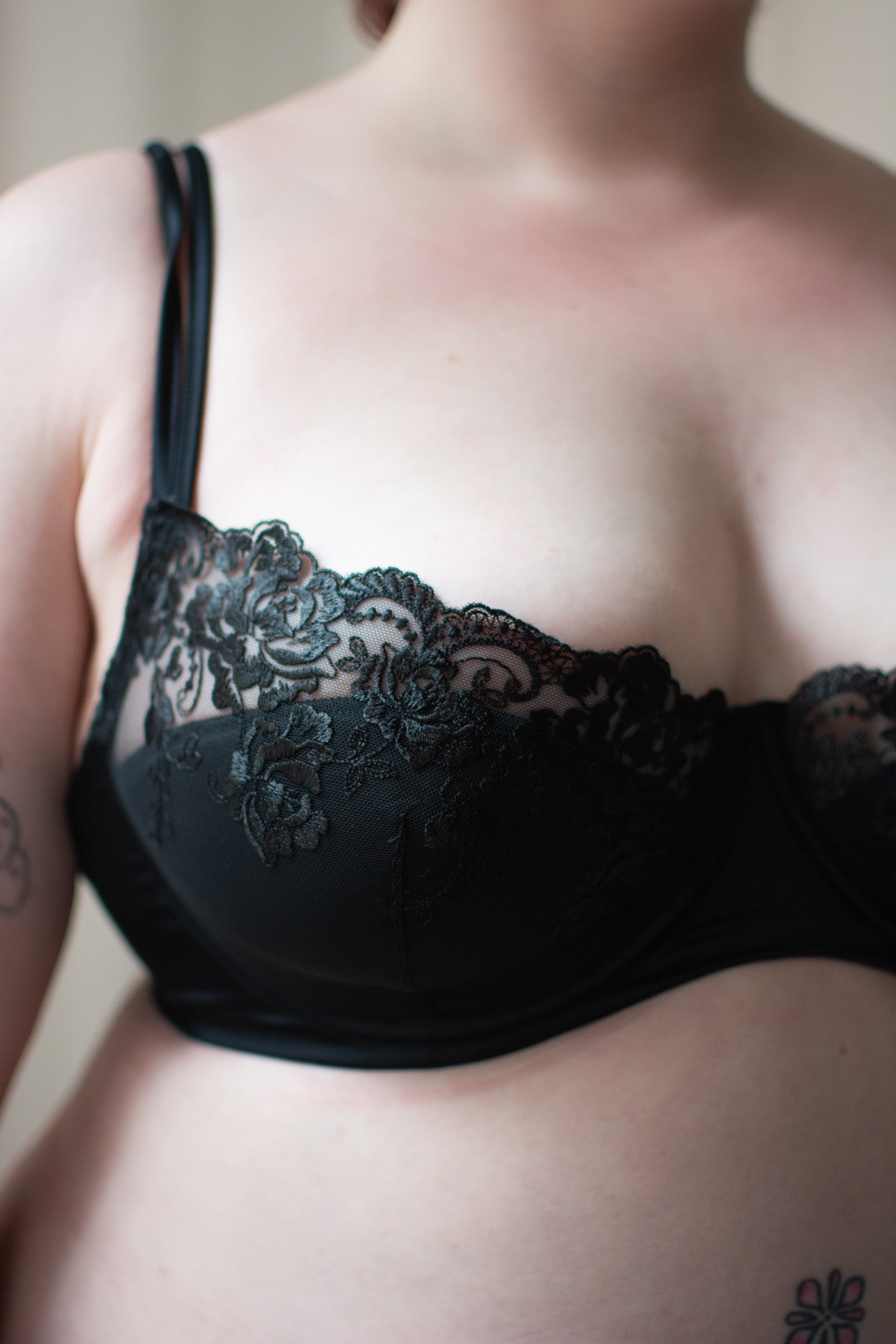 Person wearing black lace bra on neutral background.