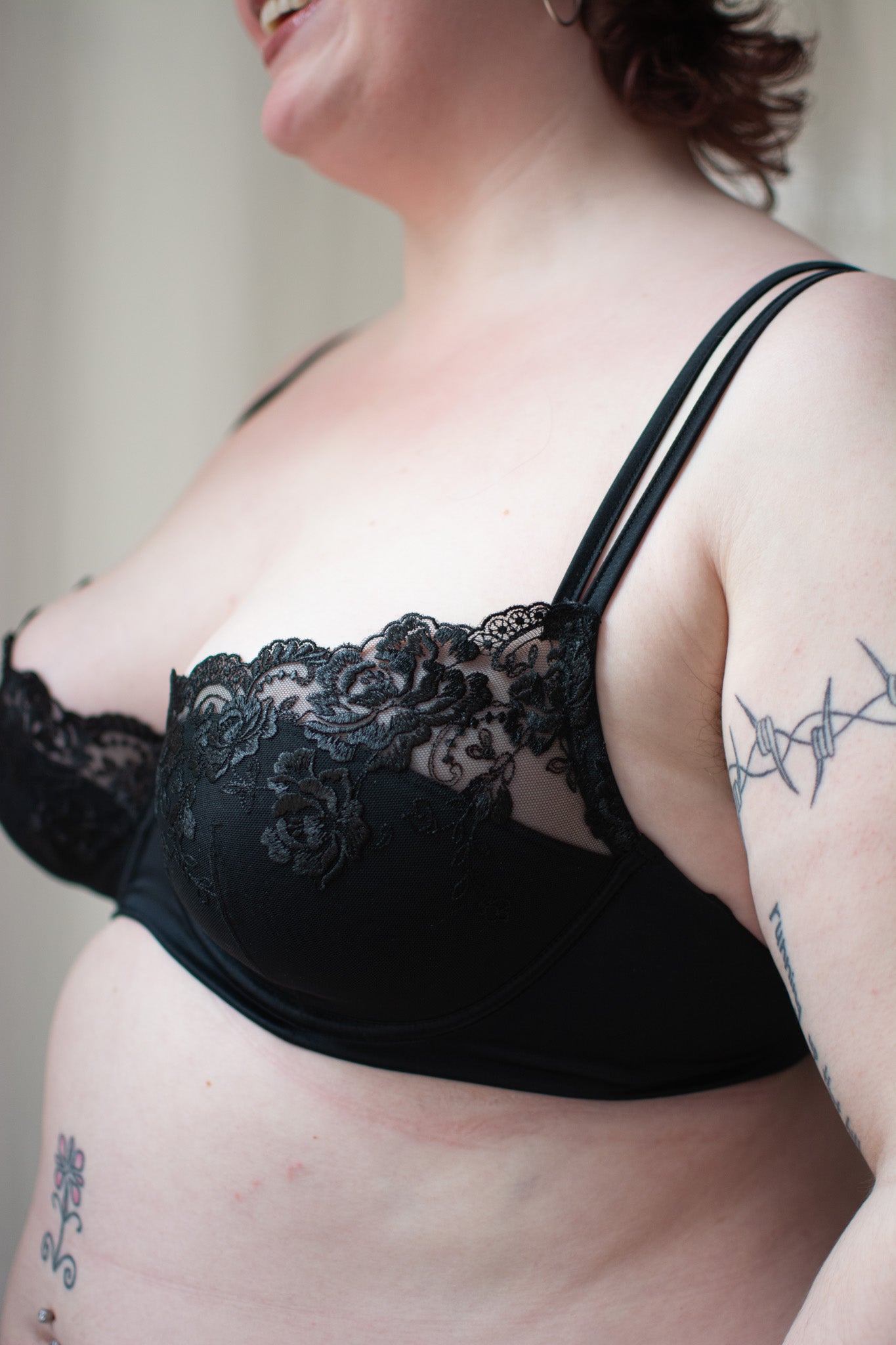 Person wearing black lace bra on neutral background.