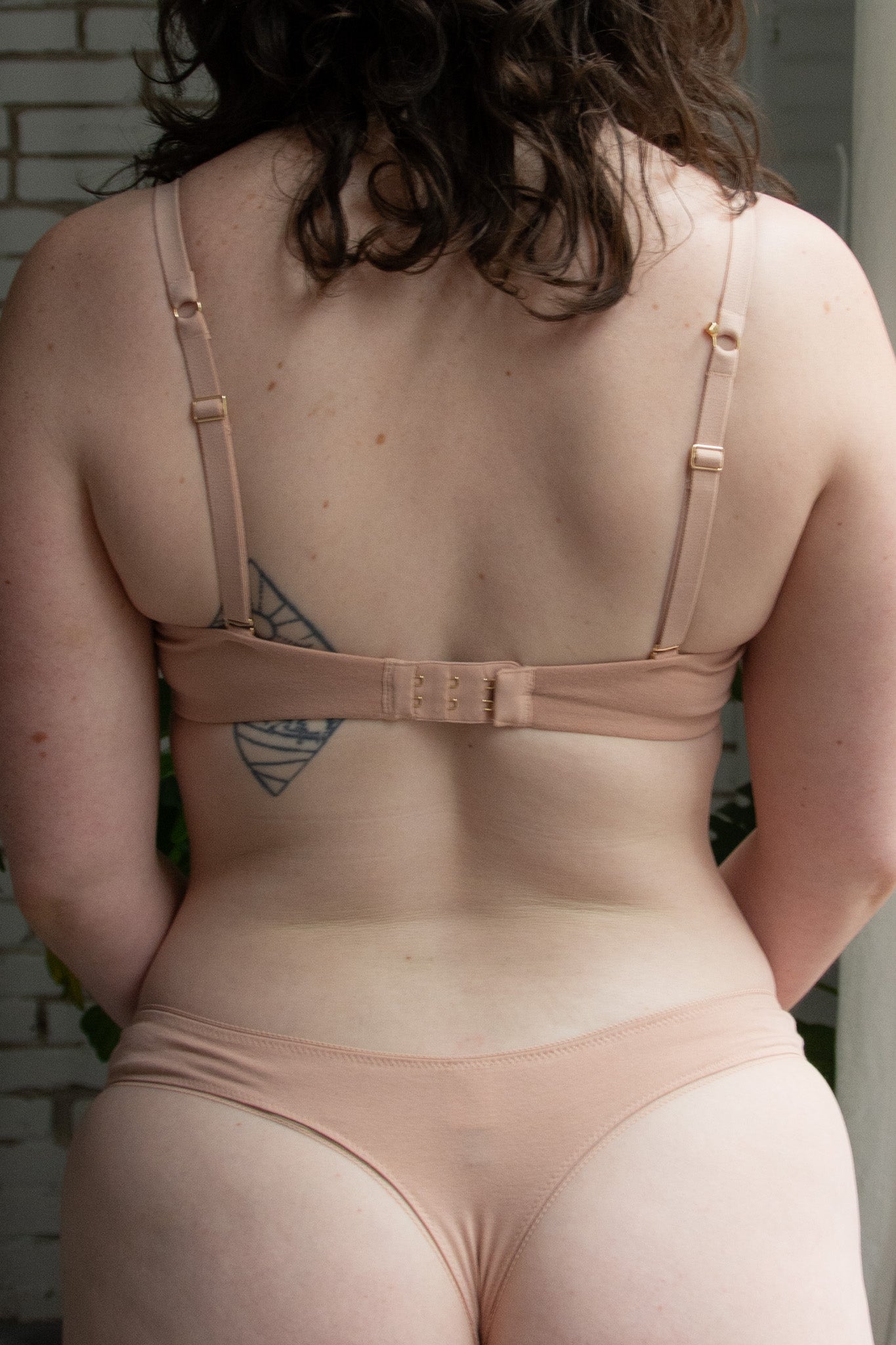 Person wearing a beige bra and panties set with a tattoo visible on the back.
