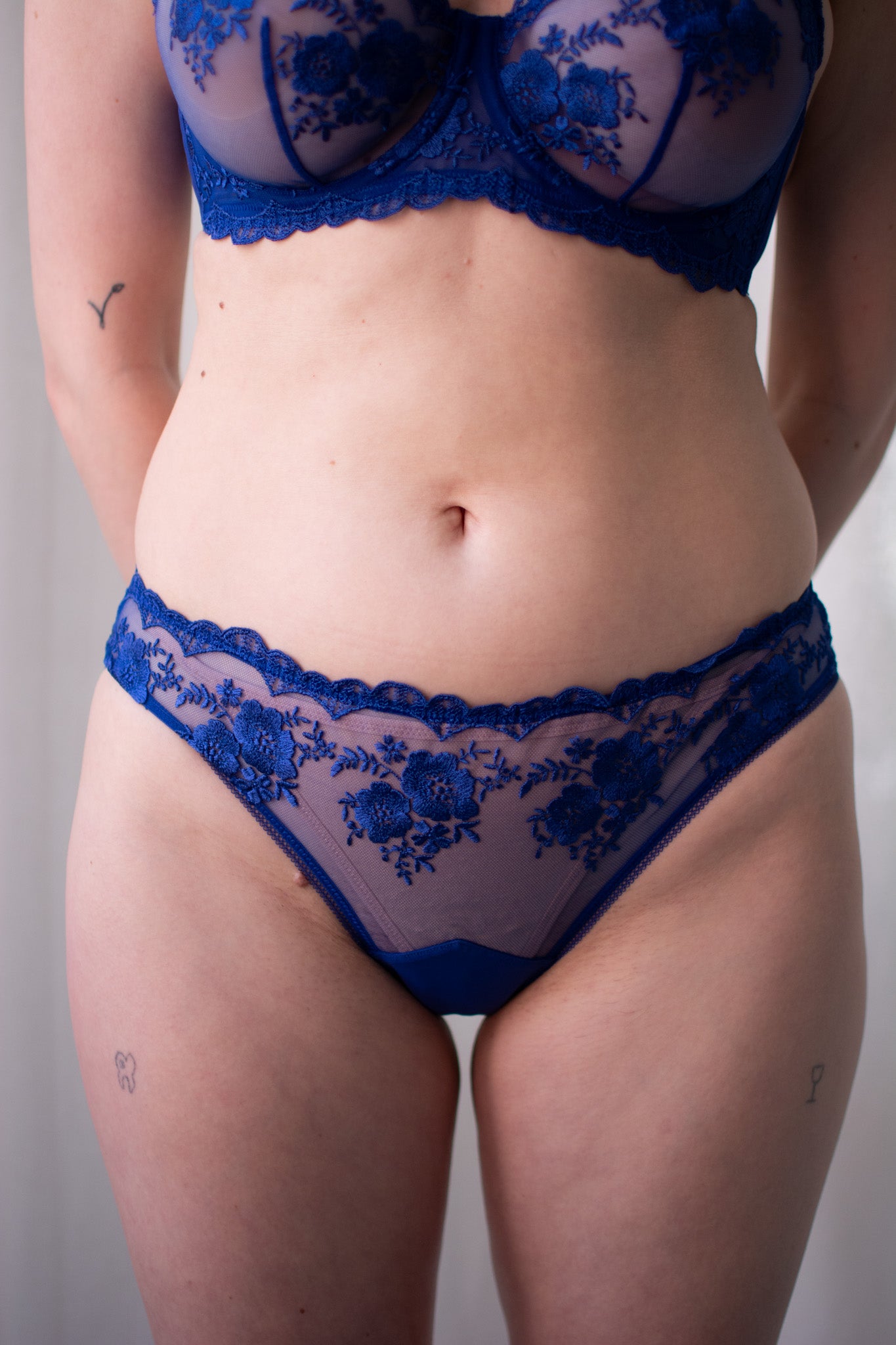 Person wearing a blue lace bra and panties set against a neutral background