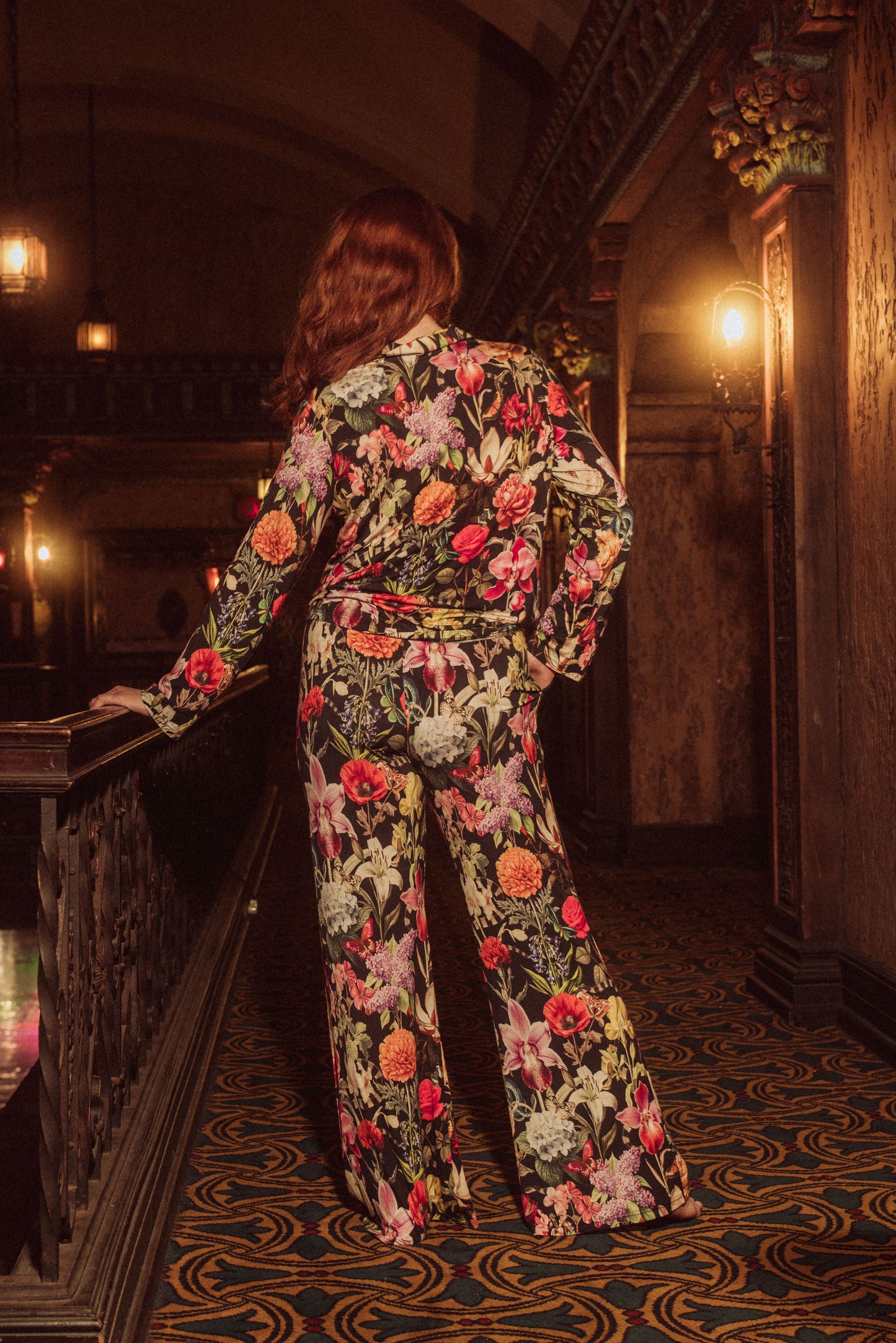 Person wearing a floral outfit standing in an ornate interior setting.