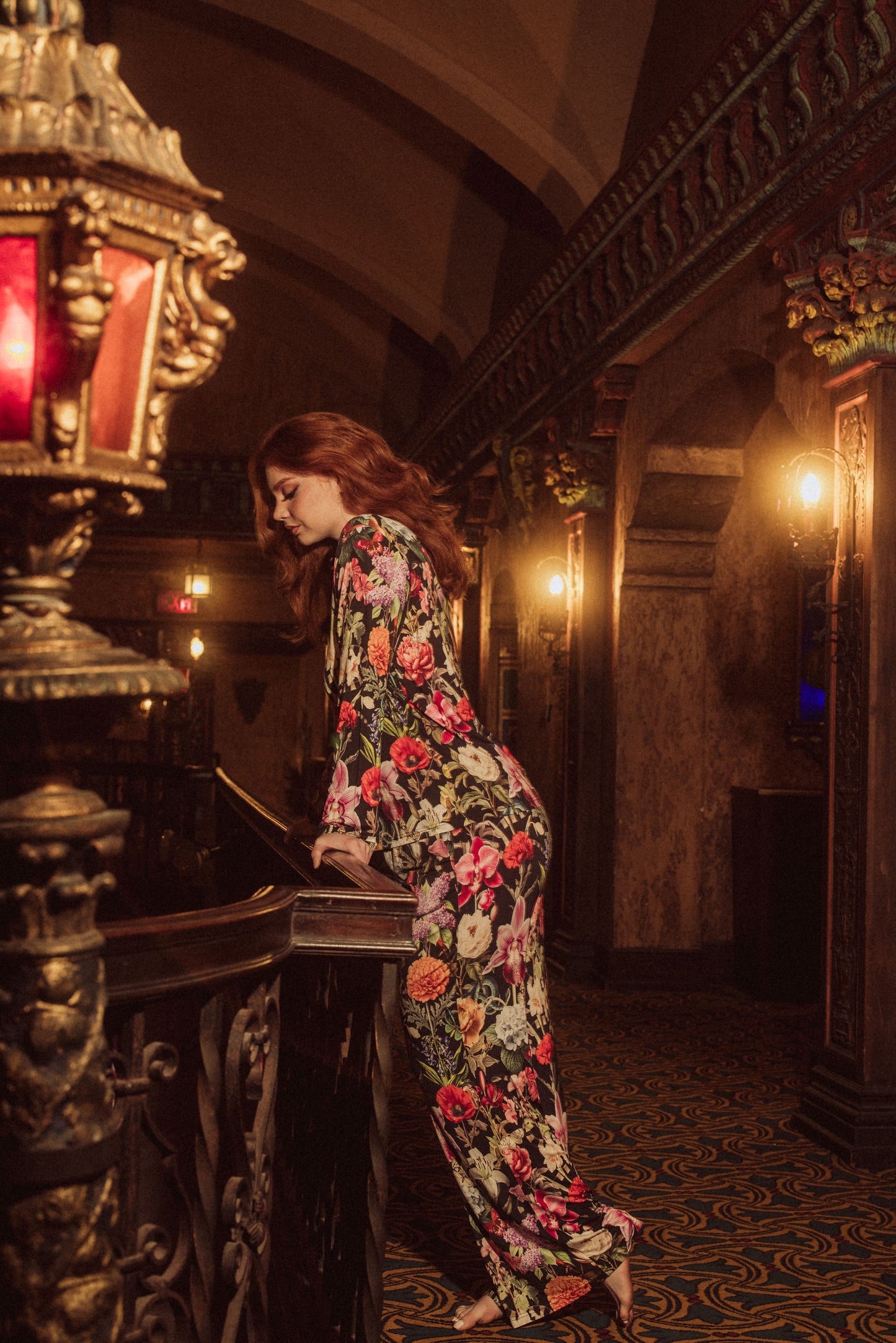 Woman in a floral dress playing a piano in an ornate room.