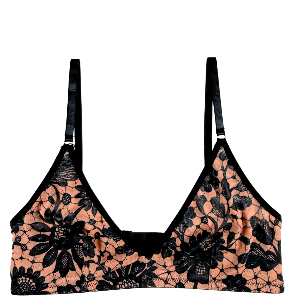 A black floral lace bralette with peach-colored mesh lining and black straps, shown against a plain white background.