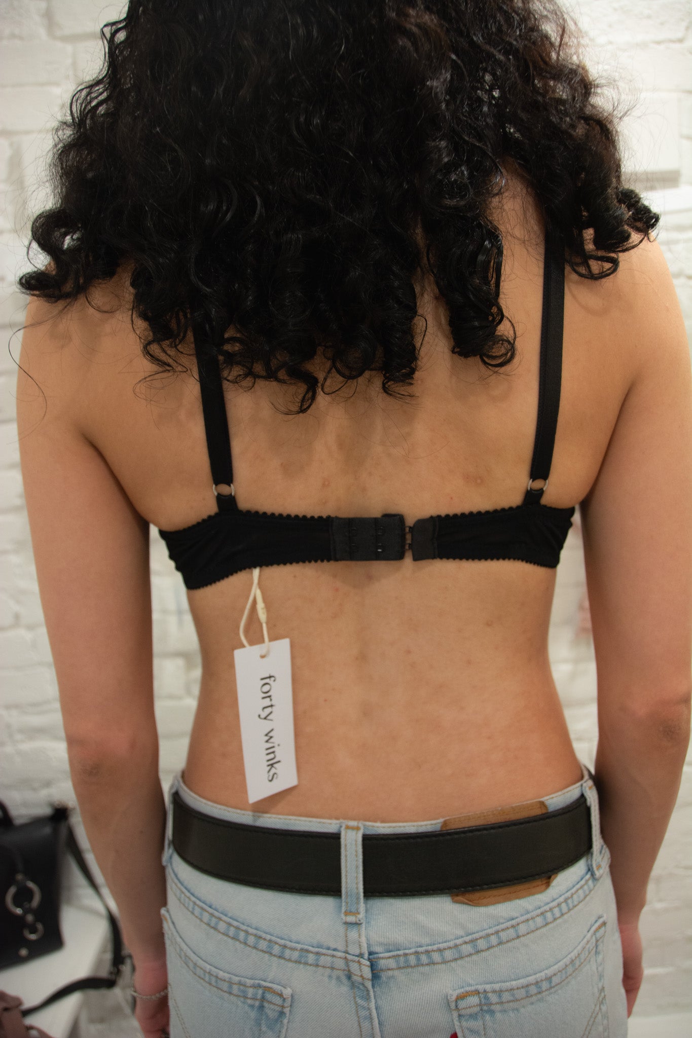 Person wearing a black bra with a visible brand tag against a white brick wall.