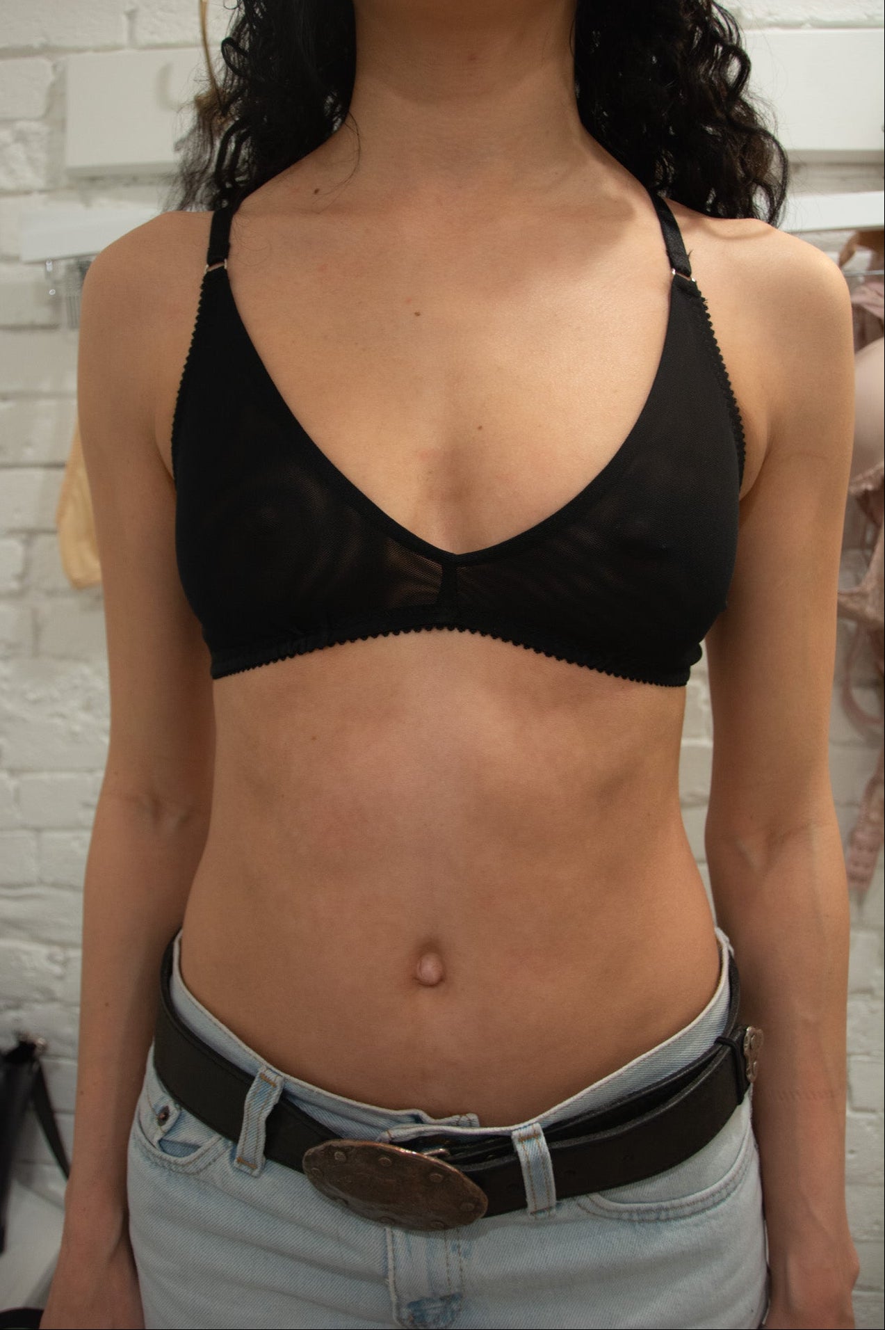 Person wearing a black bra and light blue jeans against a white brick wall.