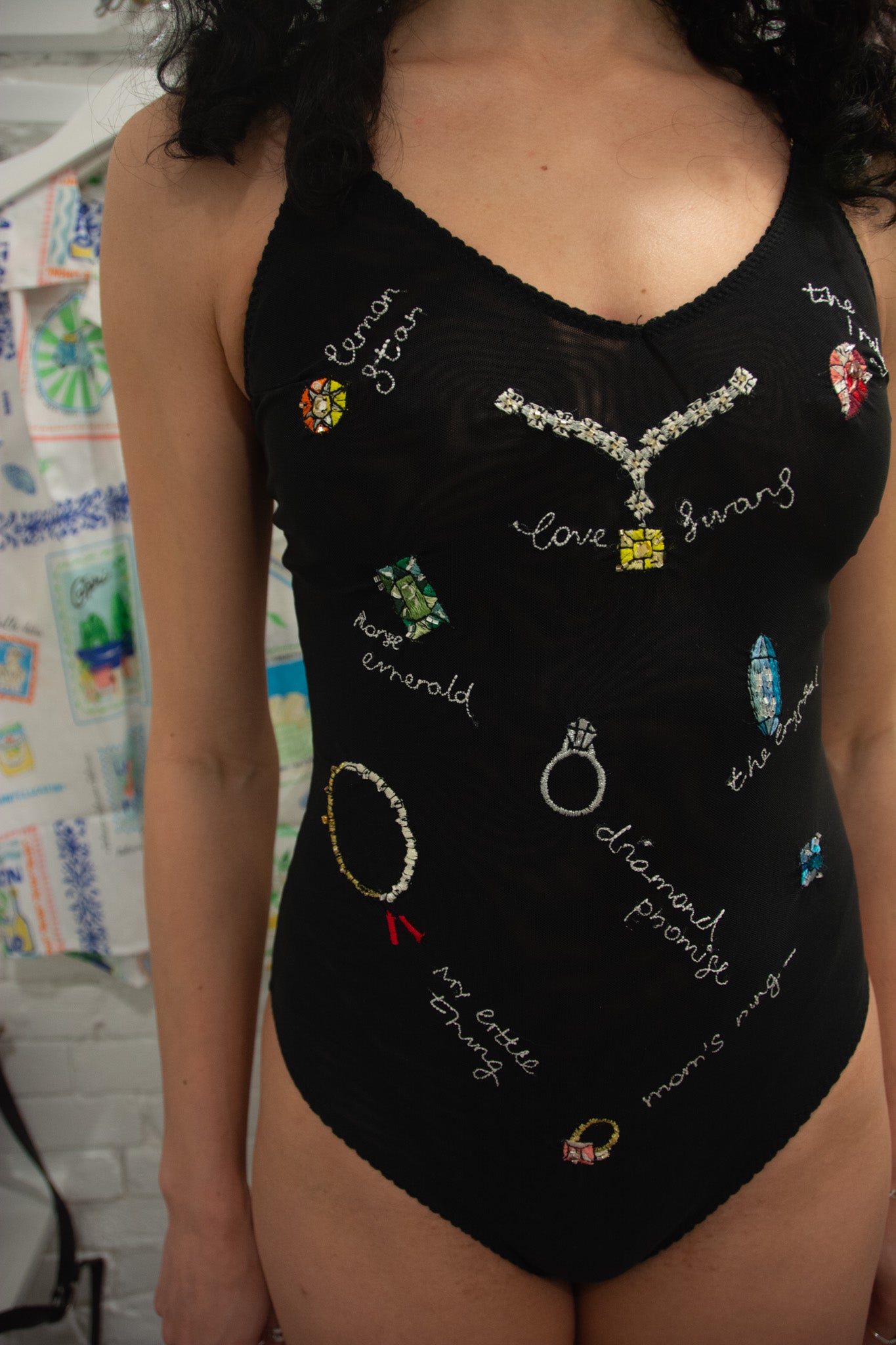 Black bodysuit with jewelry-themed embellishments worn by a person.