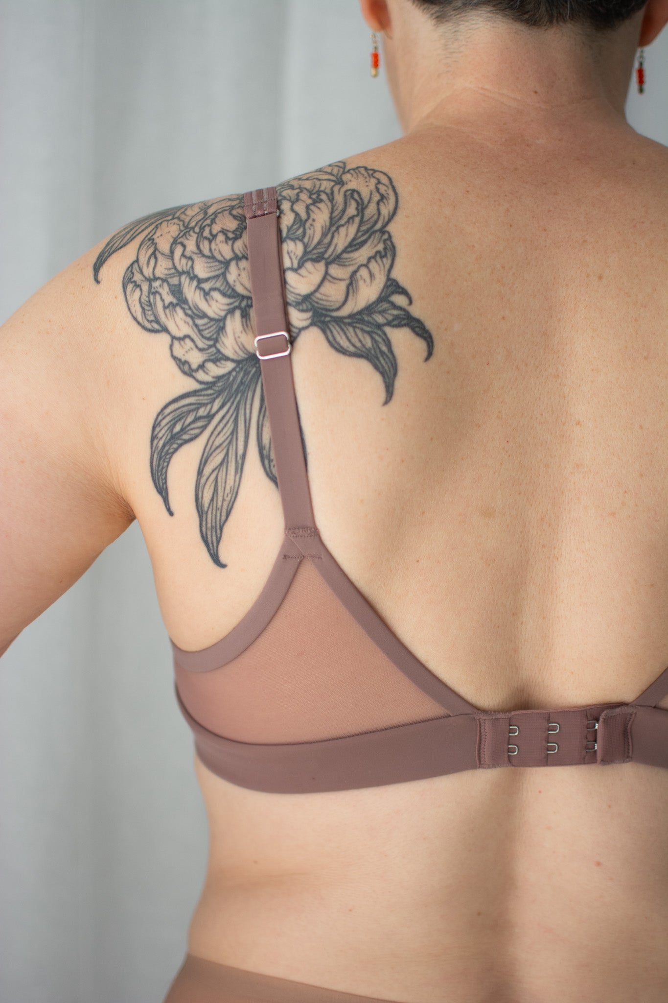 Person wearing a brown bra with a floral tattoo on the back against a neutral background
