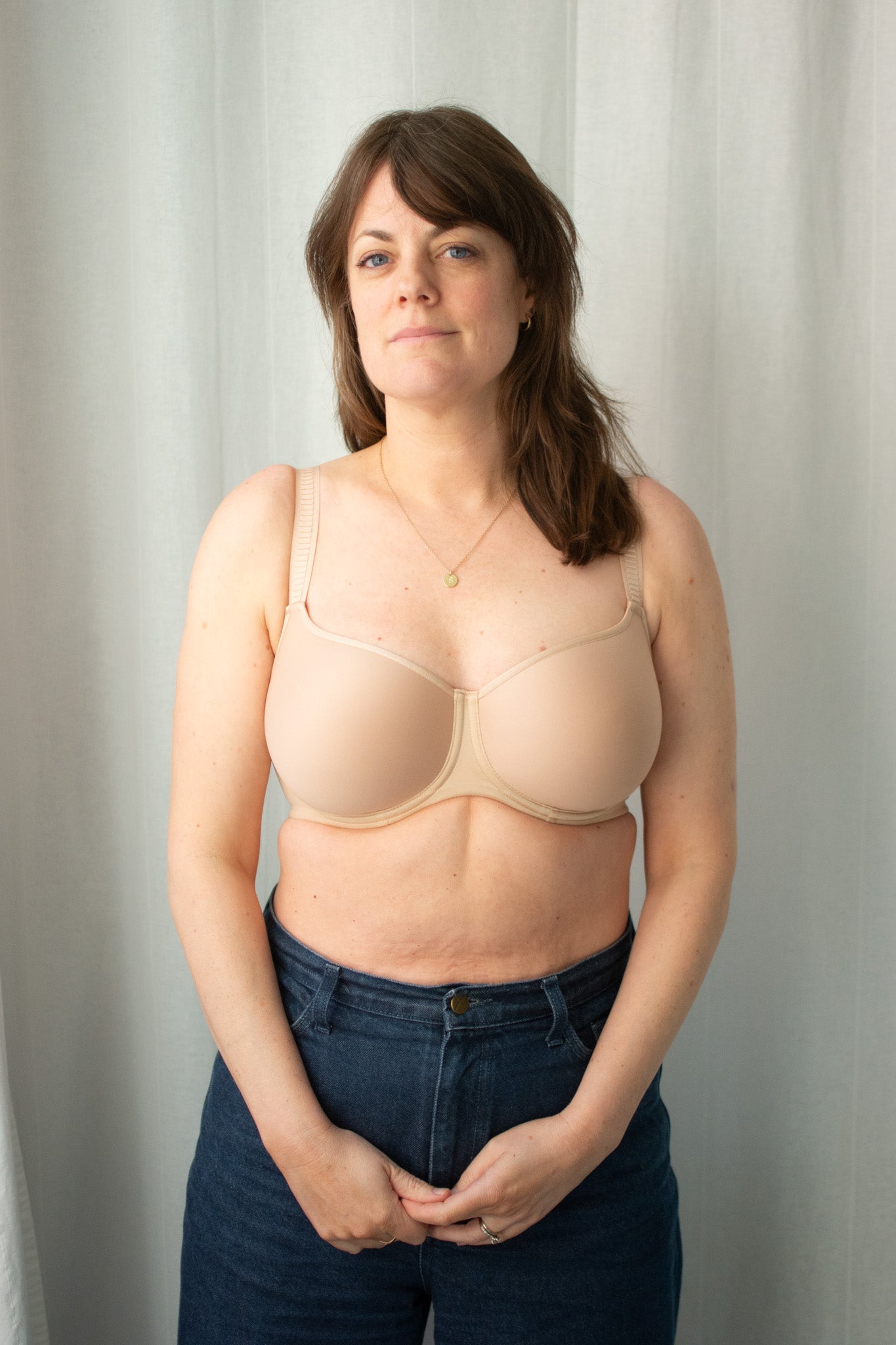 Woman wearing a beige bra and blue jeans against a plain background