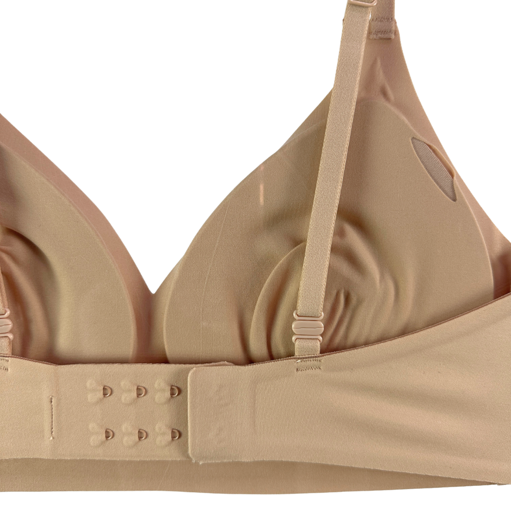 Close-up of a beige wireless underwire bra showing the adjustable shoulder straps, inner cup, and double-grommet back closure.