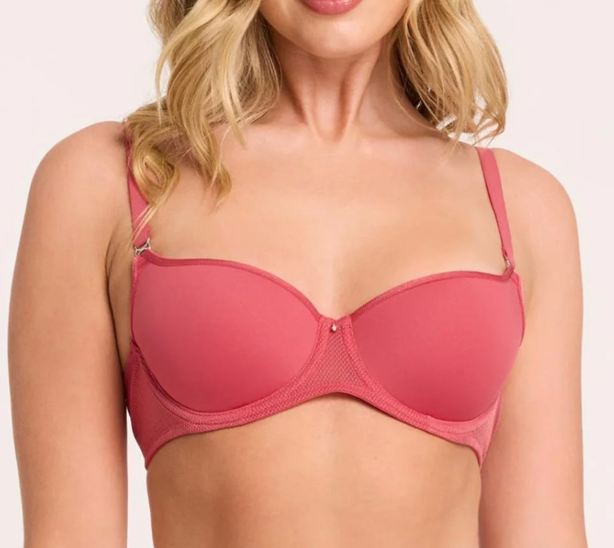 A close-up of a woman wearing a pink wireless underwire bra with mesh trim and adjustable shoulder straps, shown against a plain light background.