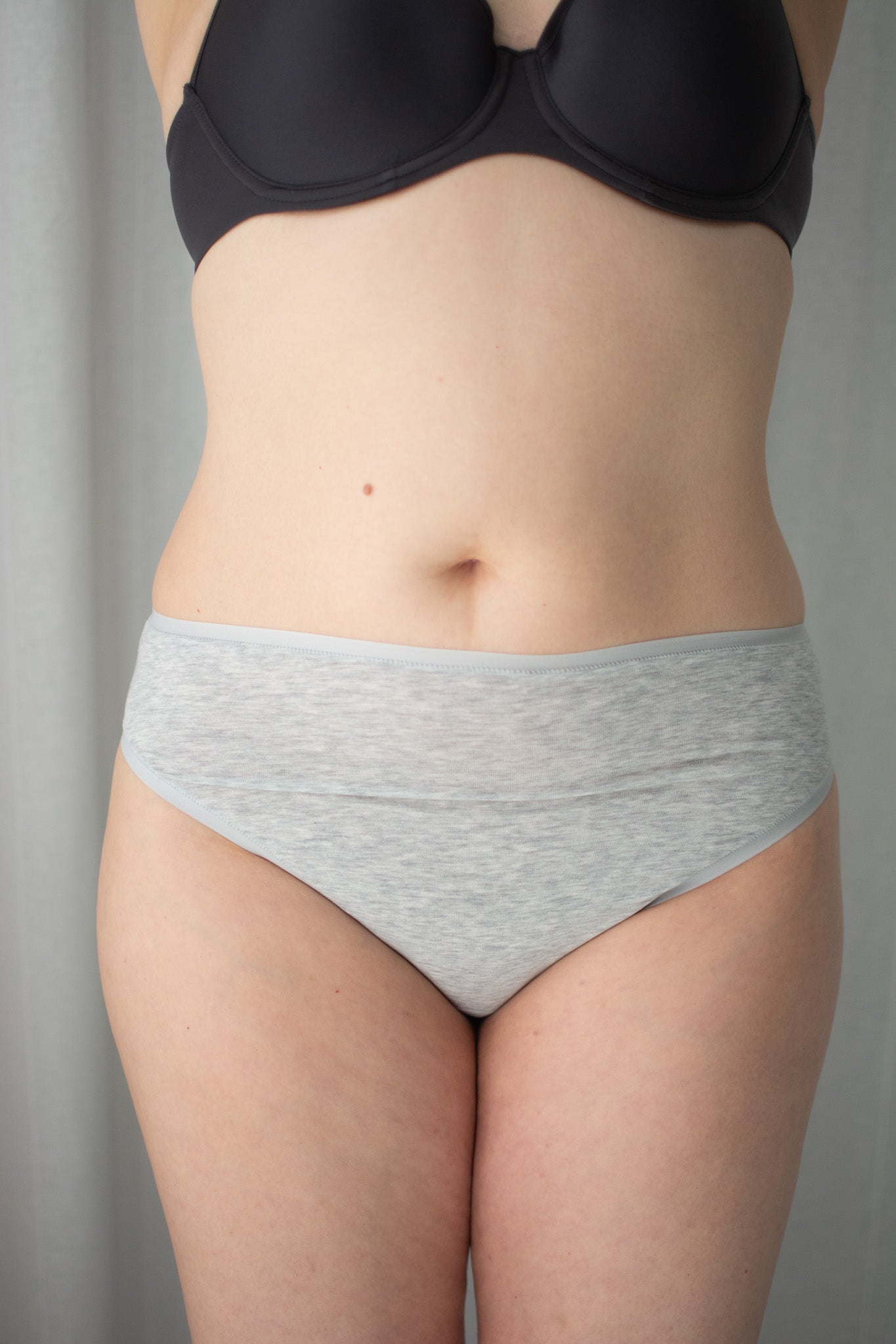Person wearing a black bra and gray underwear against a neutral background