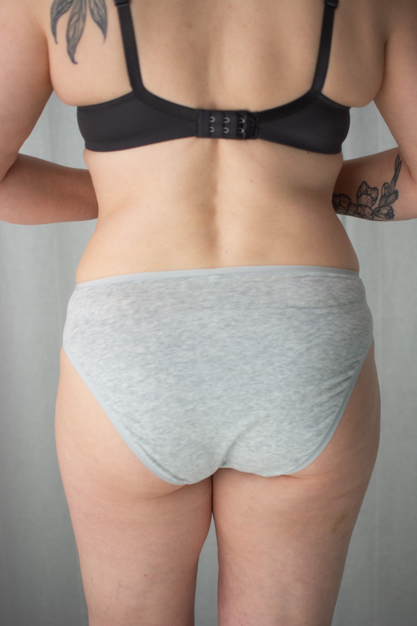 Person wearing a black bra and gray underwear against a neutral background
