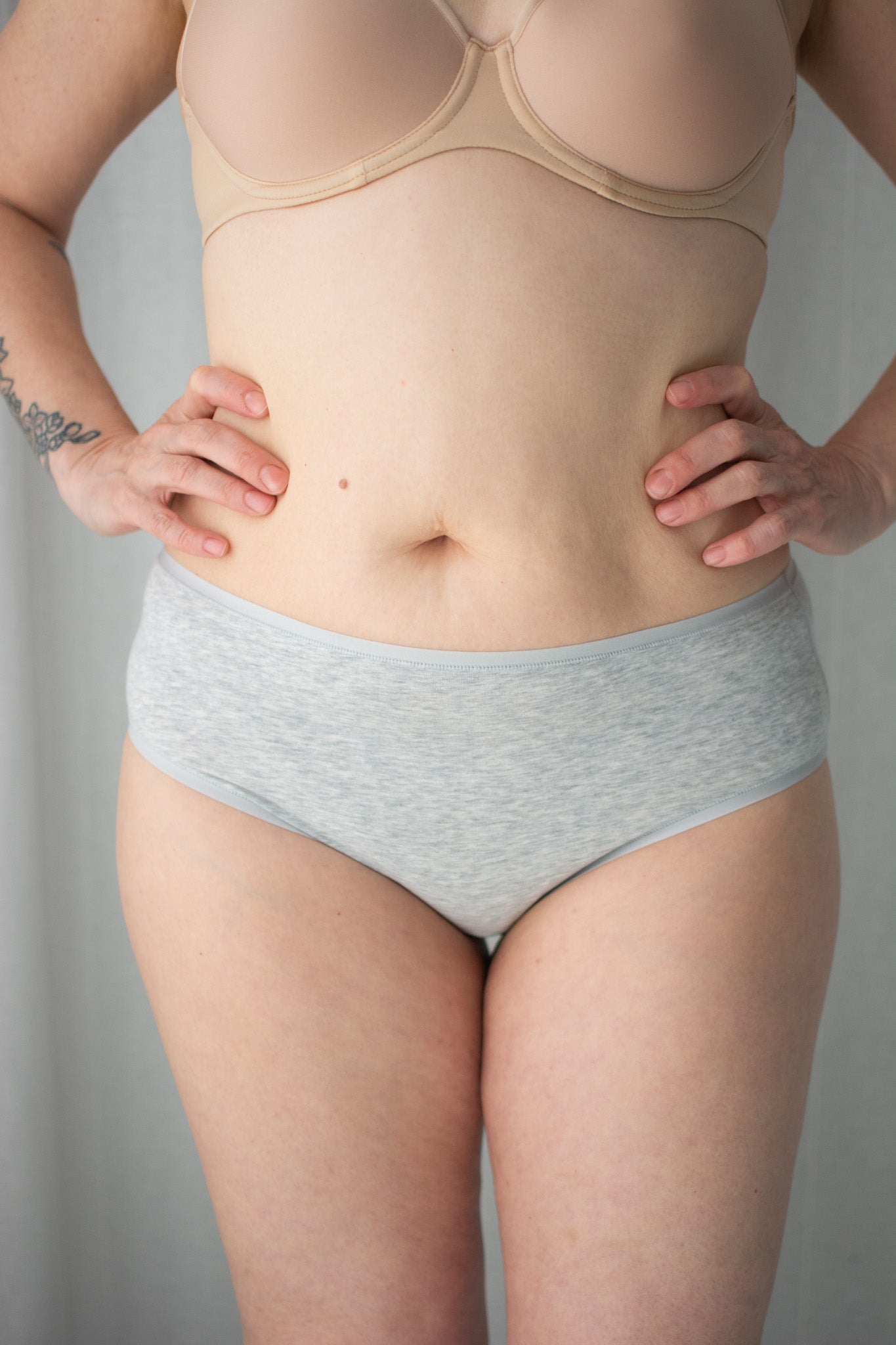 Person wearing a beige bra and gray underwear against a plain background