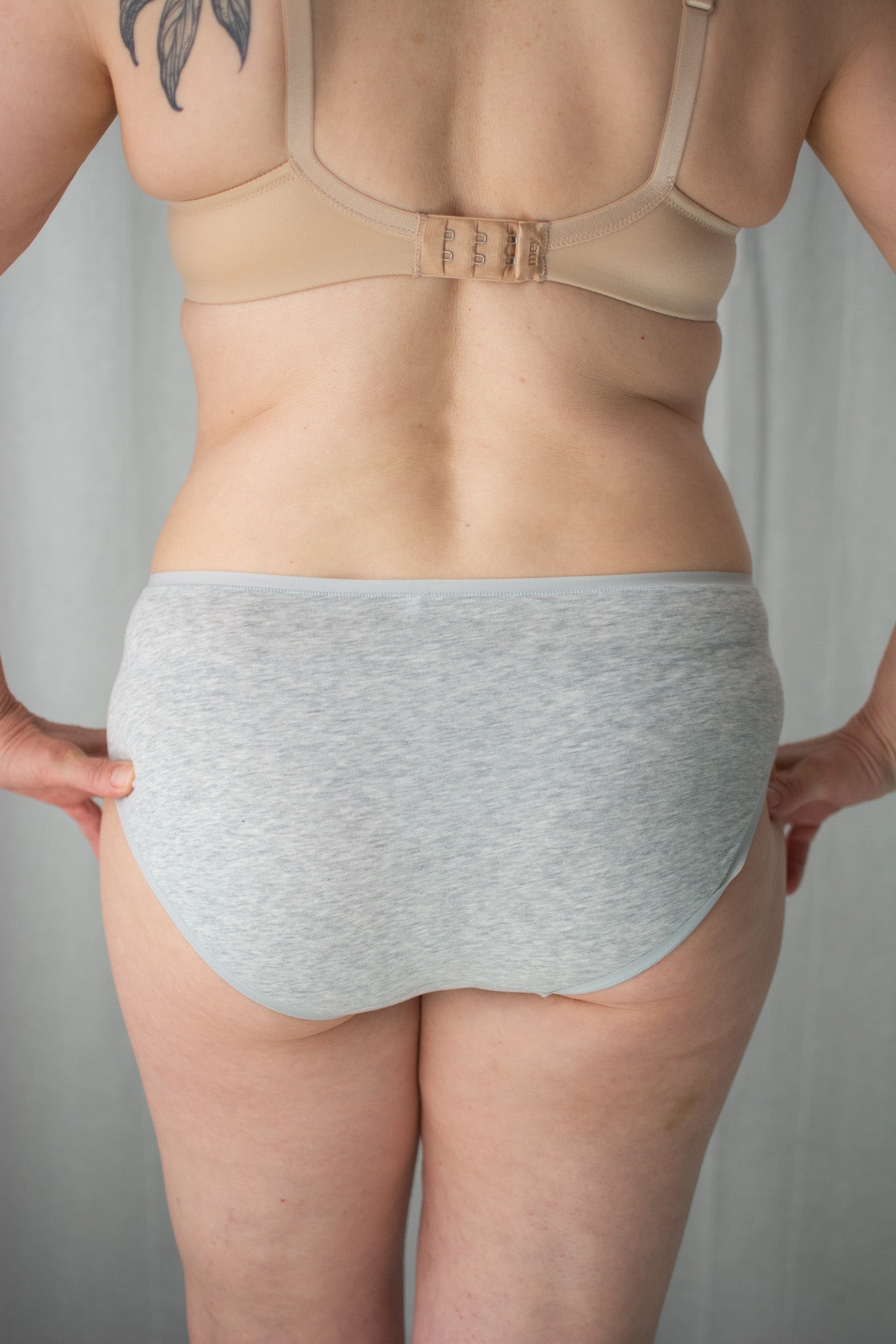 Person wearing a beige bra and gray underwear against a neutral background