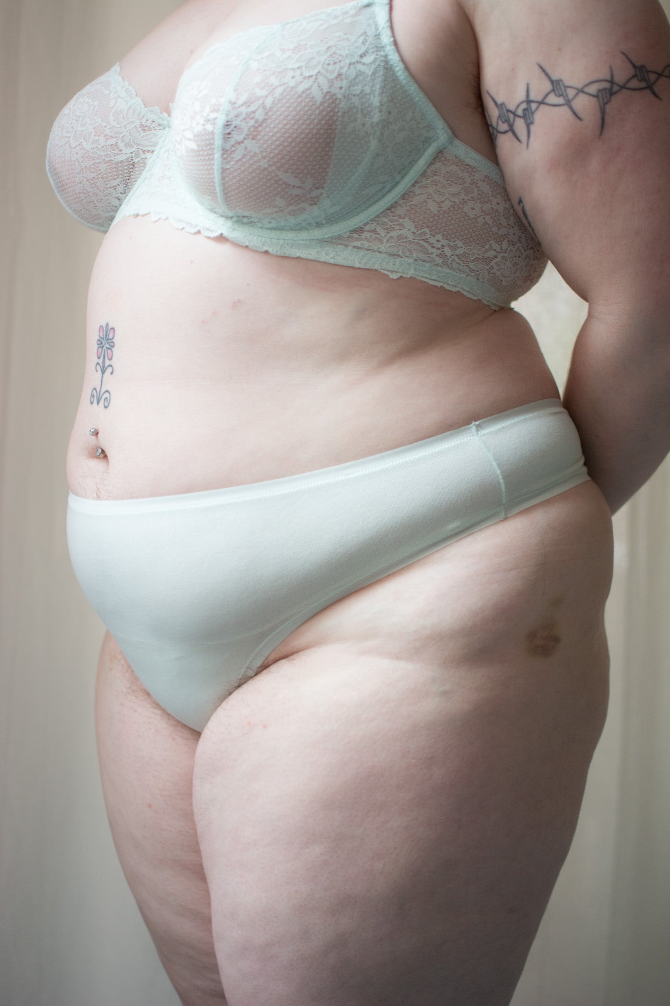 Person wearing light green bra and underwear against a neutral background.