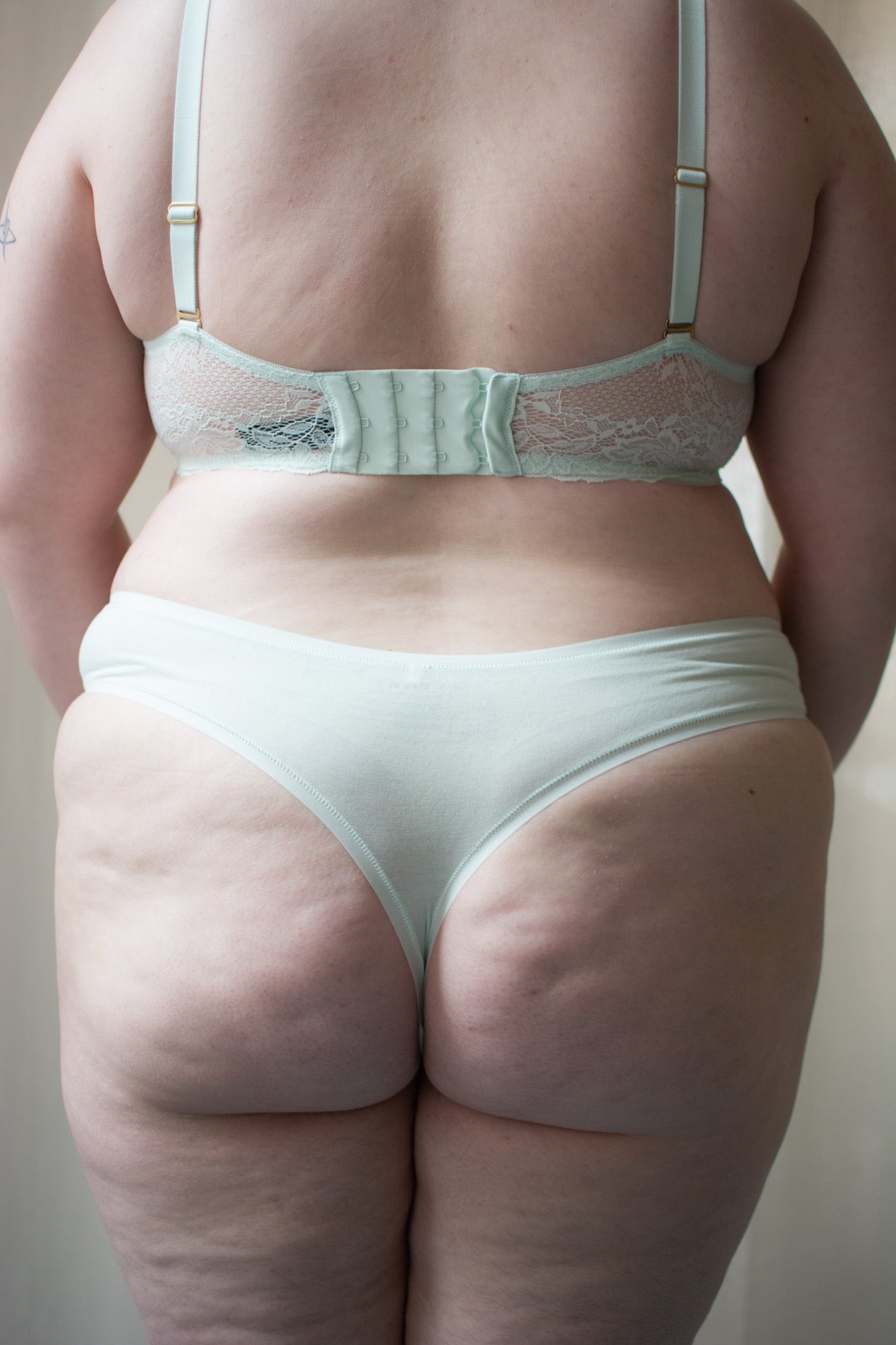 Person wearing light green bra and underwear against a neutral background.