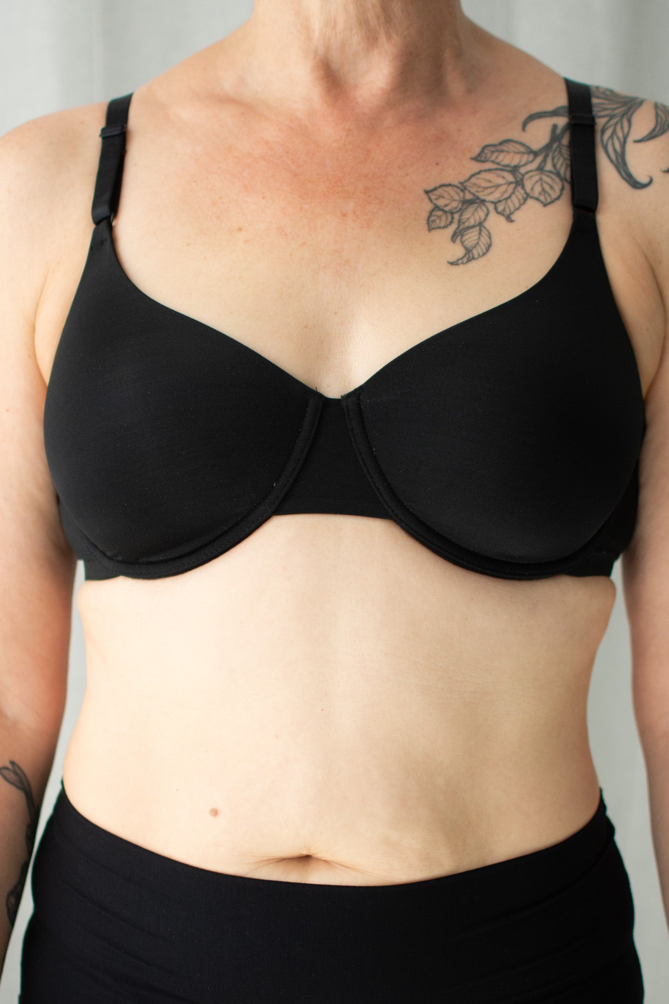 Person wearing a black bra against a neutral background