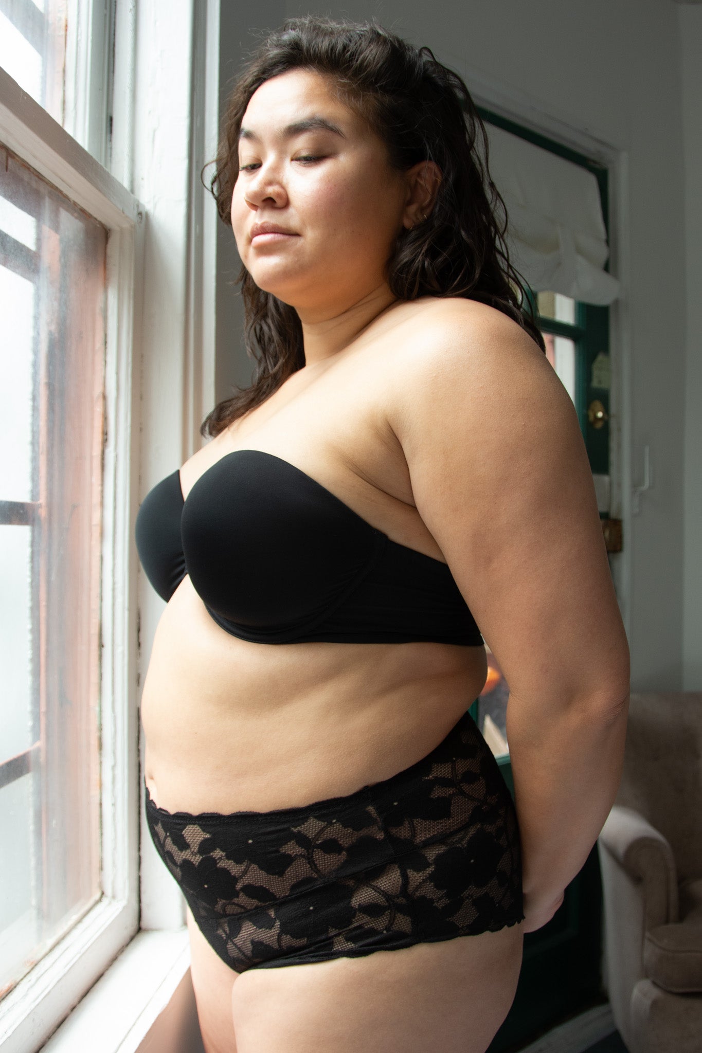 Woman wearing a black strapless top and patterned underwear in a room with a window.