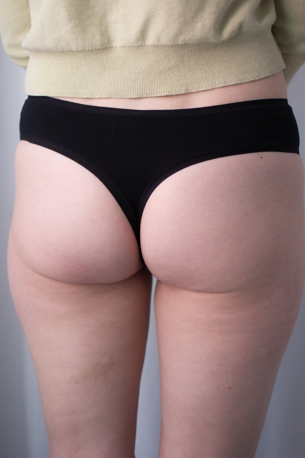 Natori bliss bare cotton thong in black, back view on a model, close-up.