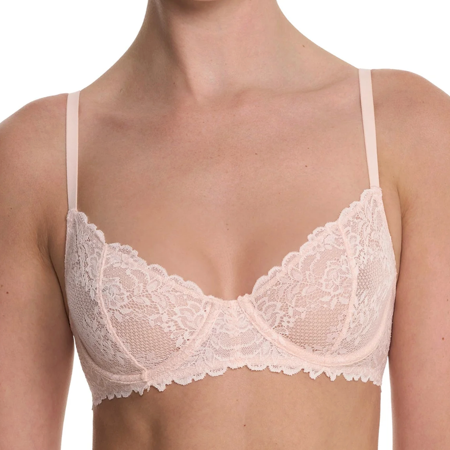 A close-up of a model wearing a light pink floral lace bra with thin straps and a scalloped underwire design, shown against a plain white background.